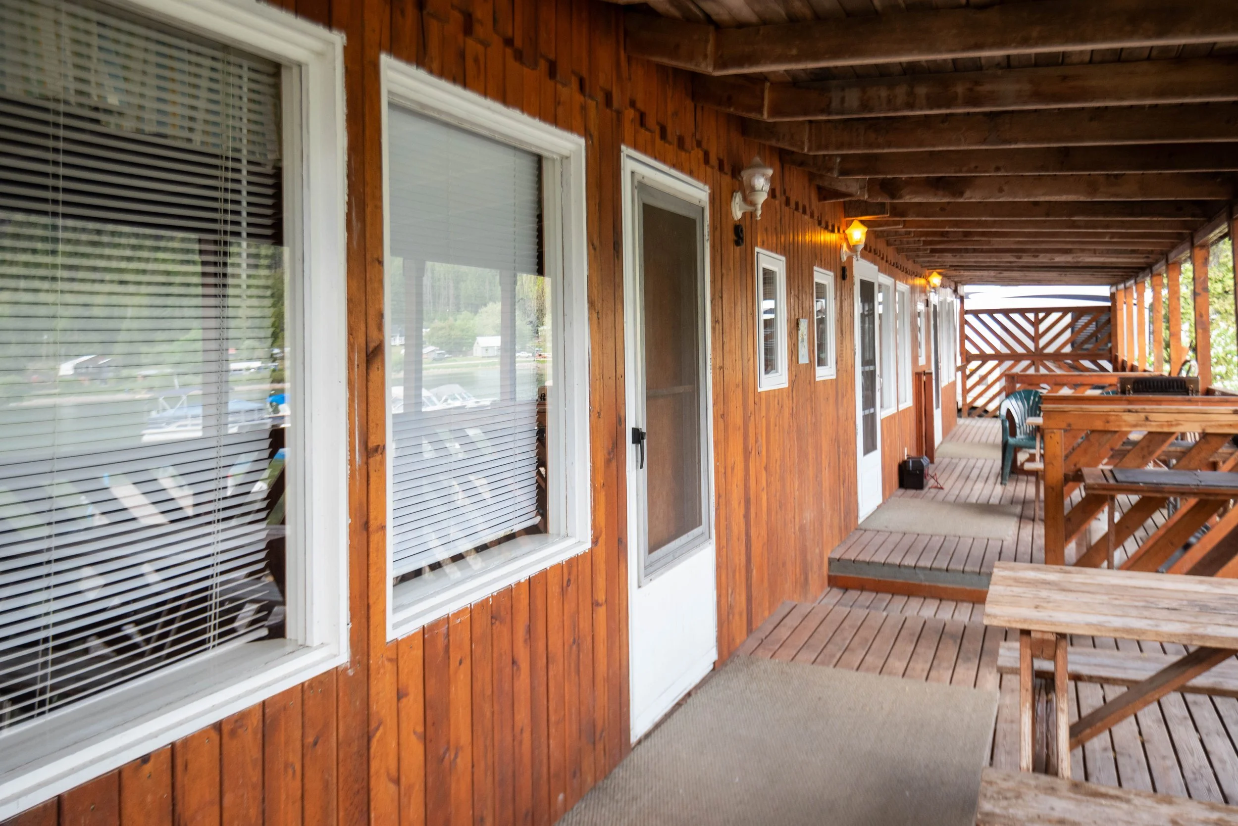 Wooden porch with several windows and a door, outdoor seating with a table and chairs, and string lights hanging beneath the roof.