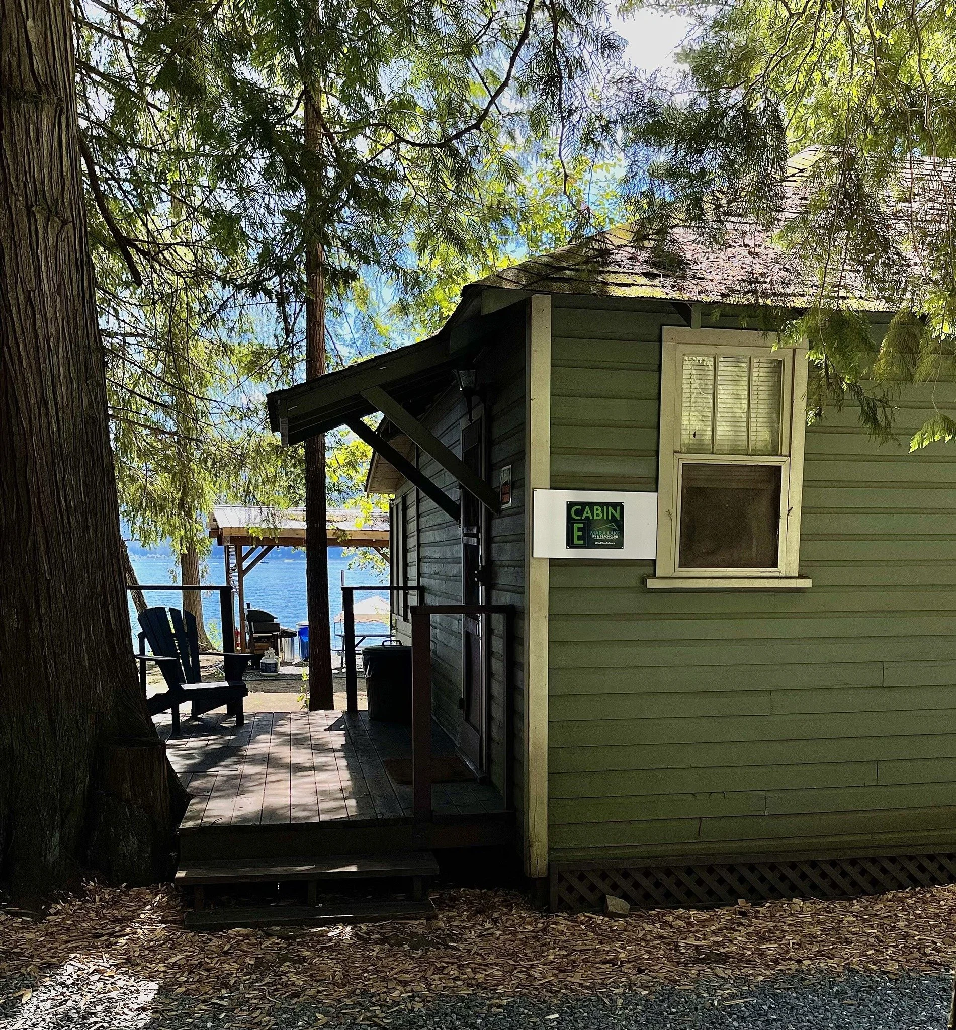 A small house on a porch overlooking a lake, surrounded by trees with green leaves.