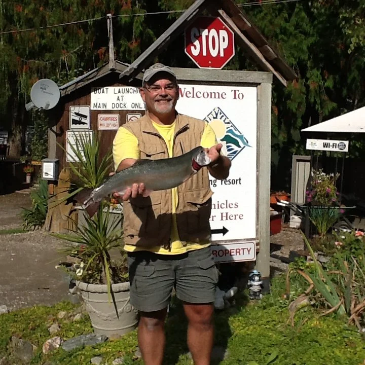 A man holding a large fish in front of a sign at a fishing resort.