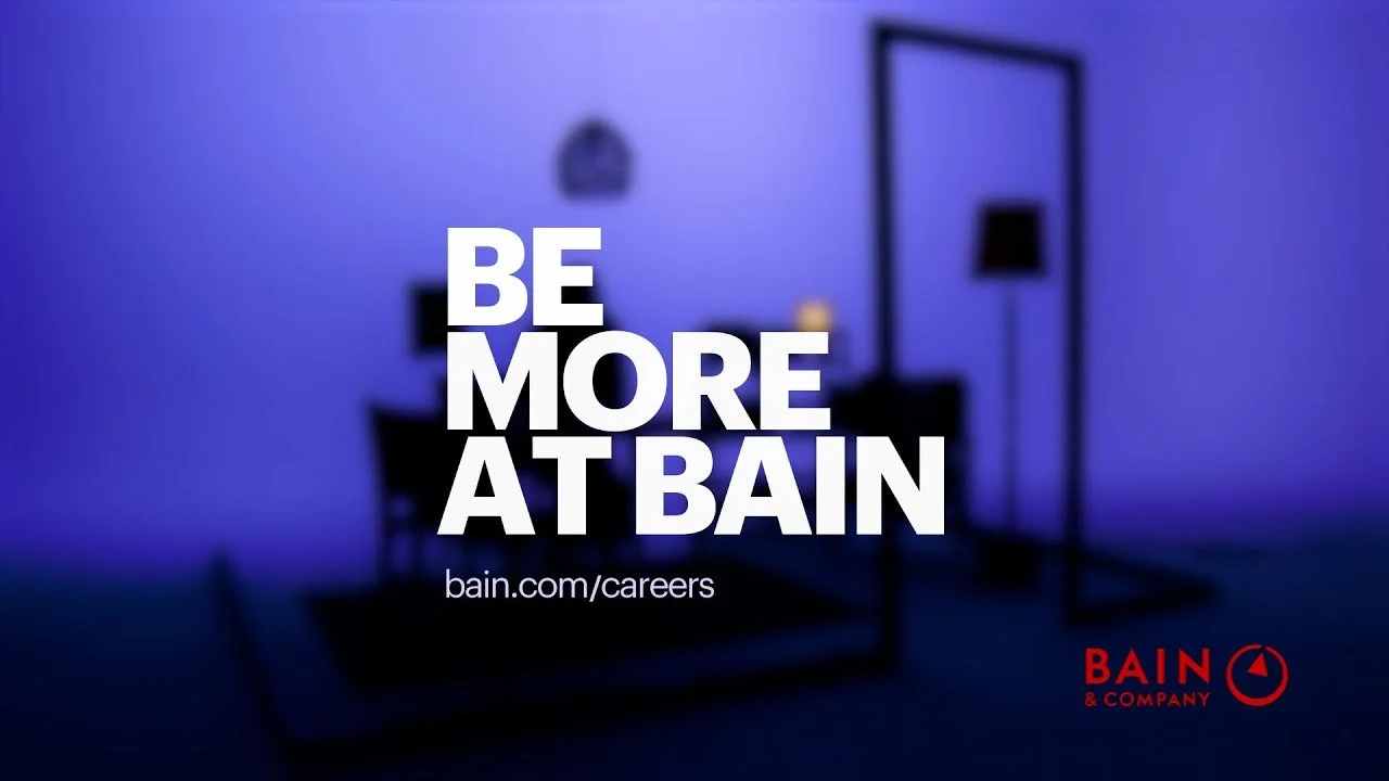 Blurred interior of a room with a chair, a lamp, and a mirror, with text stating "Be More At Bain" and a website link, along with Bain & Company's logo.