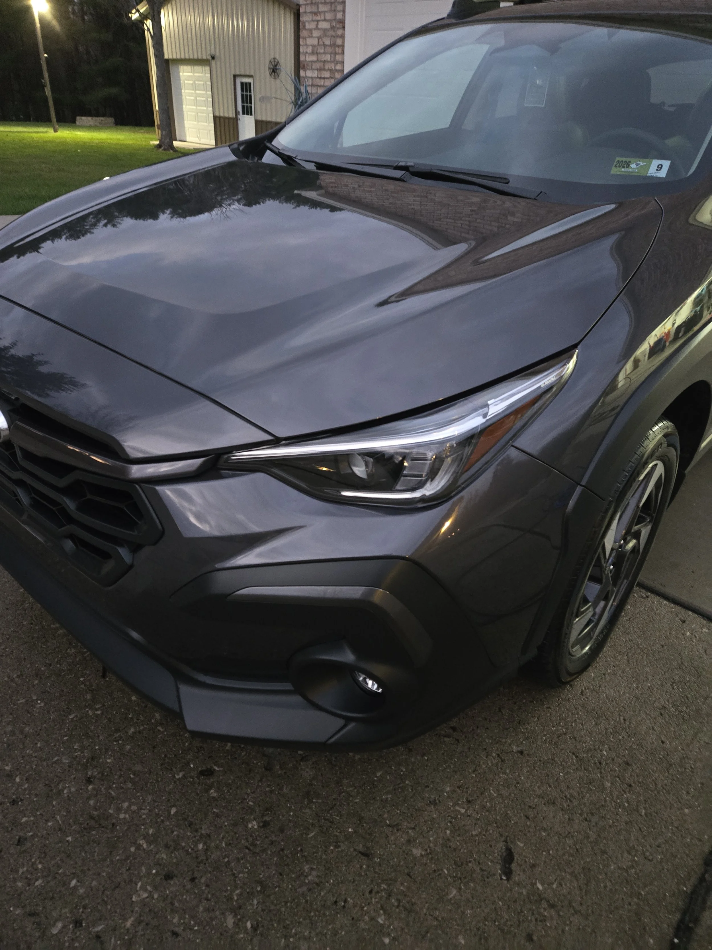 Gray car parked on a driveway with a building and trees in the background.