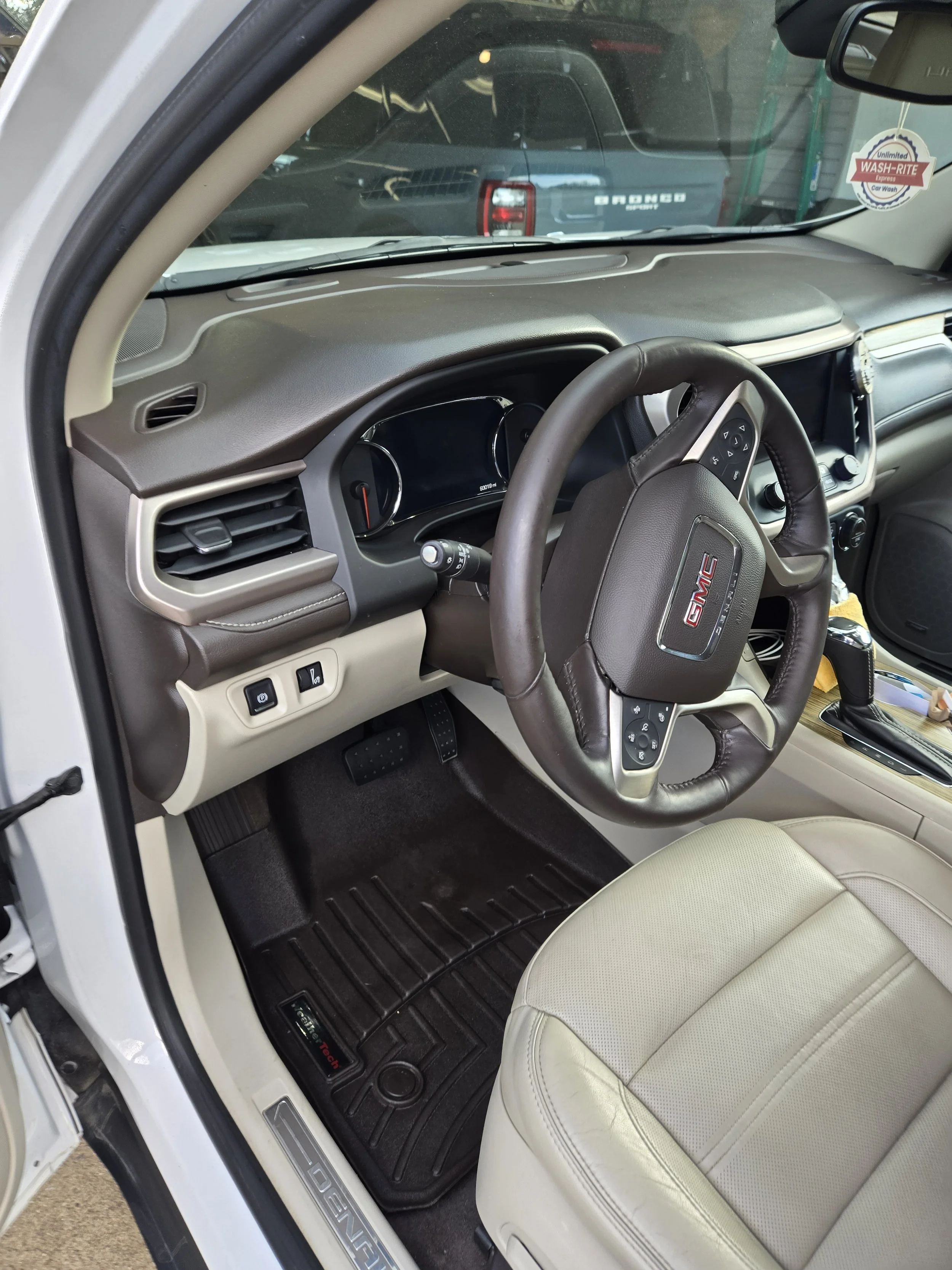 Interior of a GMC vehicle showing the steering wheel, dashboard, driver's seat, and floor mat.