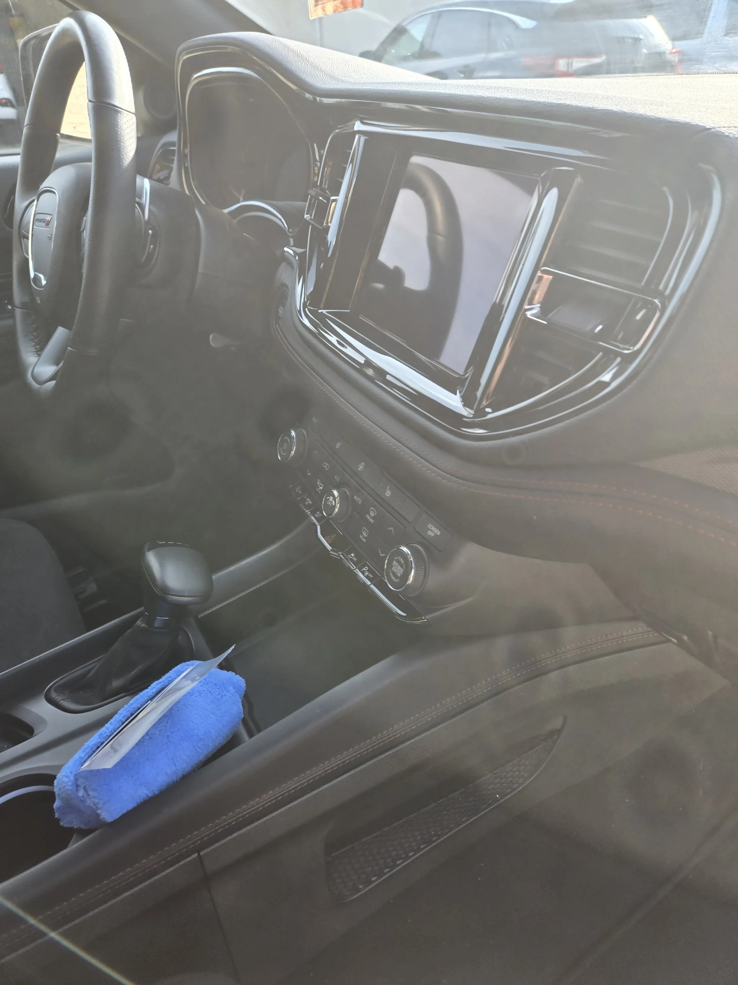 Interior of a vehicle showing the dashboard, steering wheel, gear shifter, and a blue furry item on the center console.