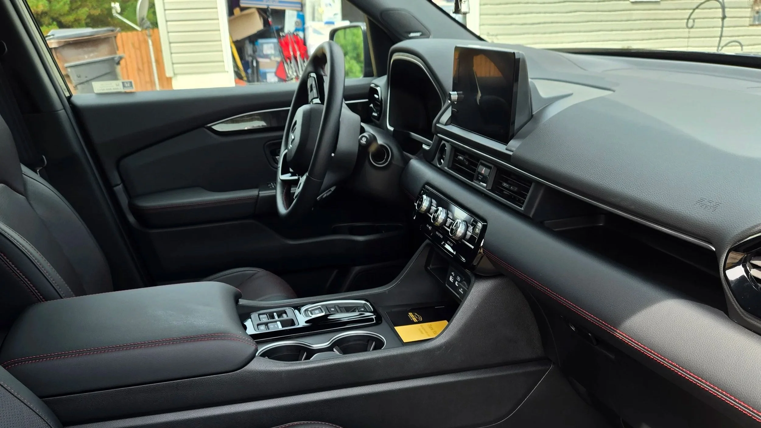 Interior of a modern vehicle showing the dashboard, steering wheel, center console with gear shifter and controls, and a partially visible driver's seat.