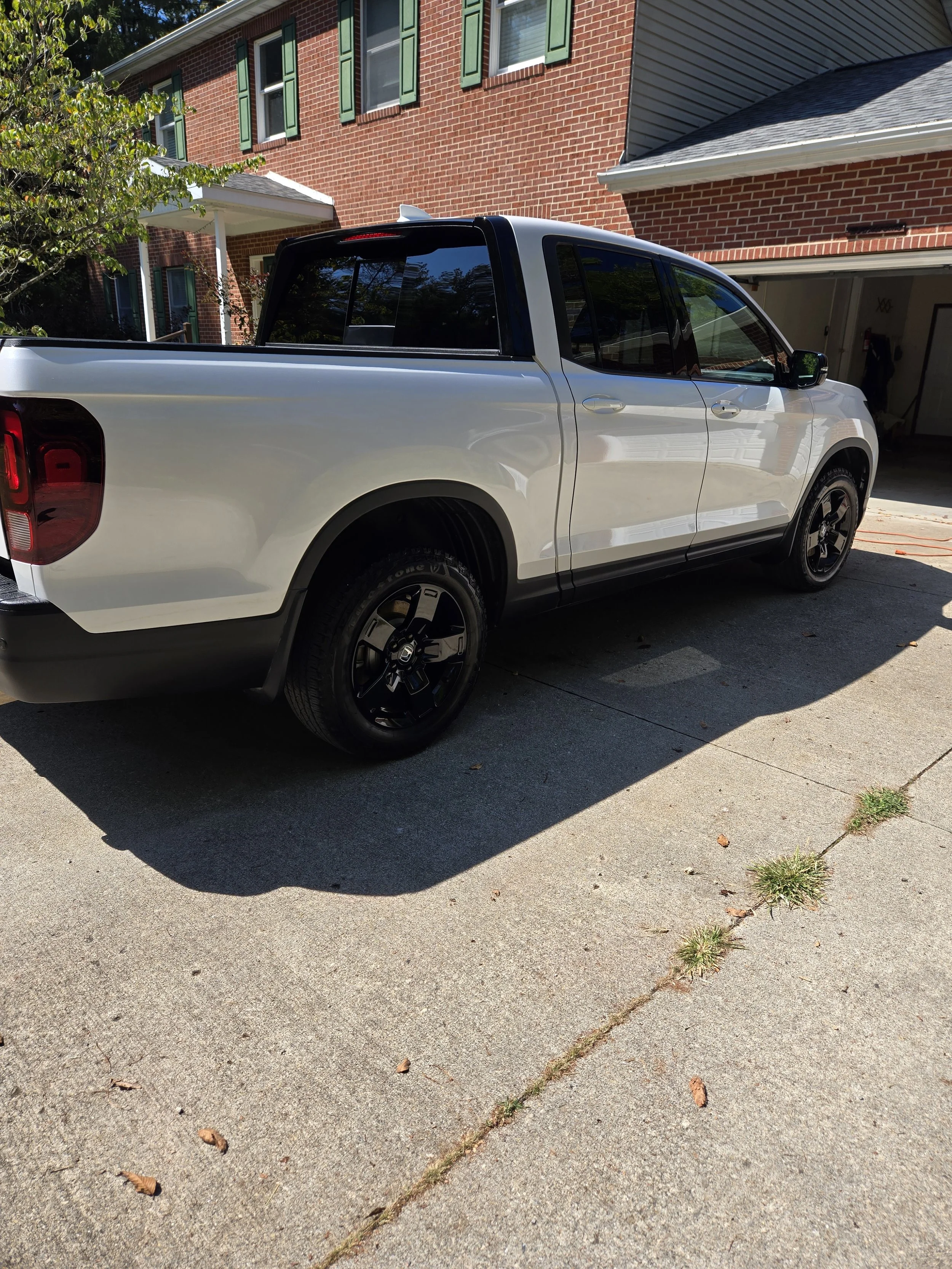 A white pickup truck parked in a driveway next to a brick house with green shutters and a garage.