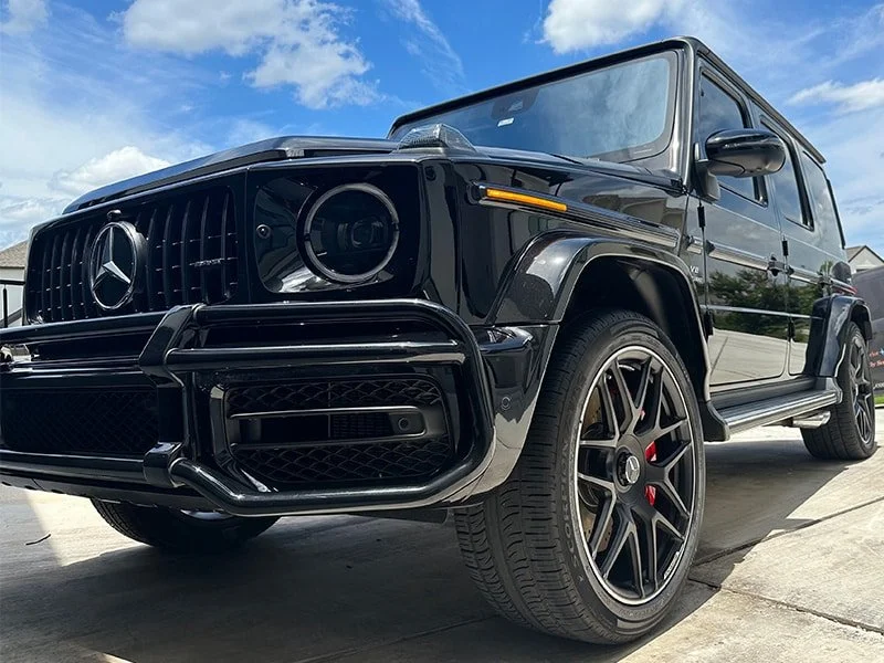 Black Mercedes-Benz G-Class SUV parked outdoors with a blue sky and some houses in the background.