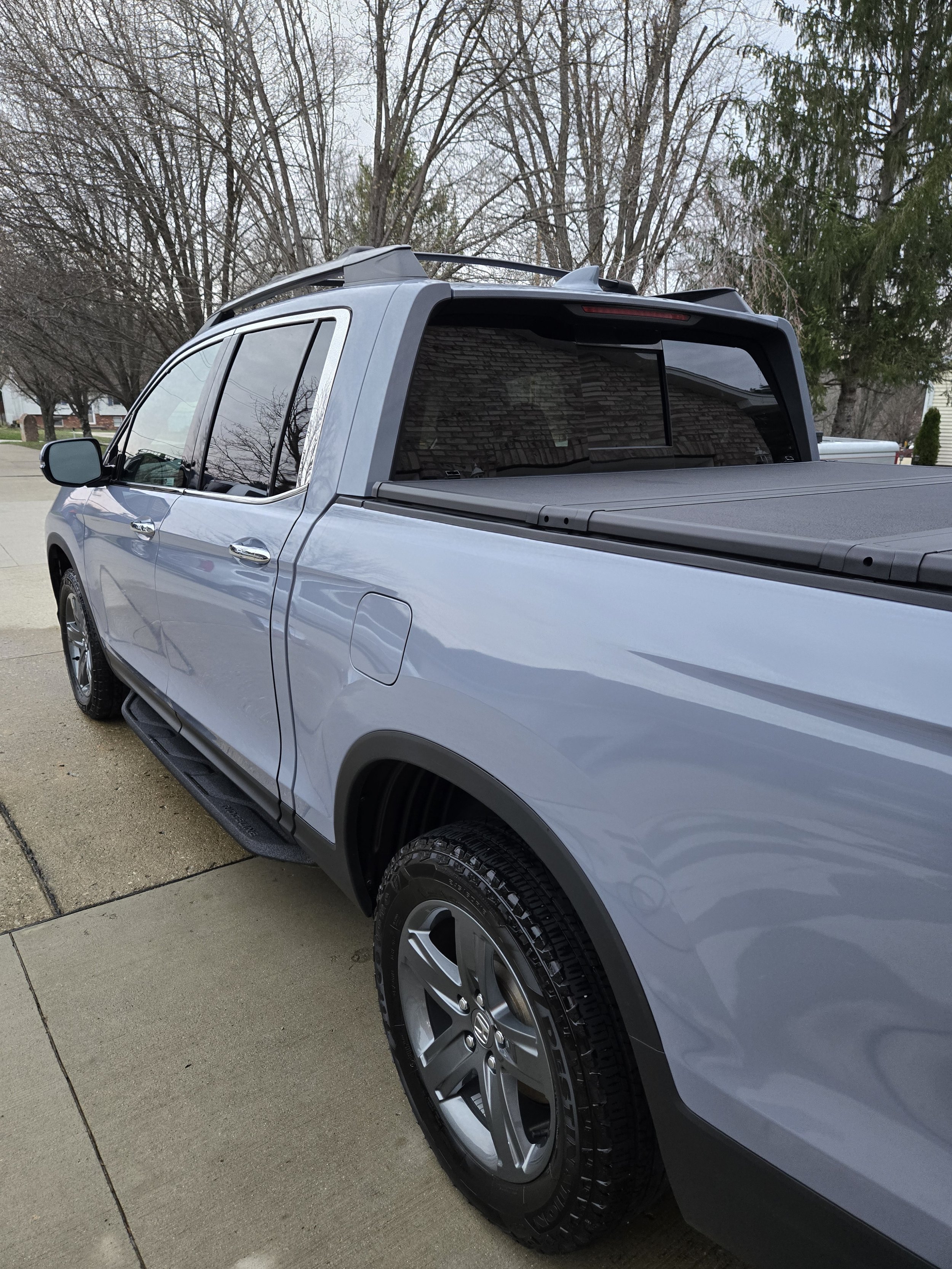 Gray pickup truck parked on a concrete driveway with trees in the background.