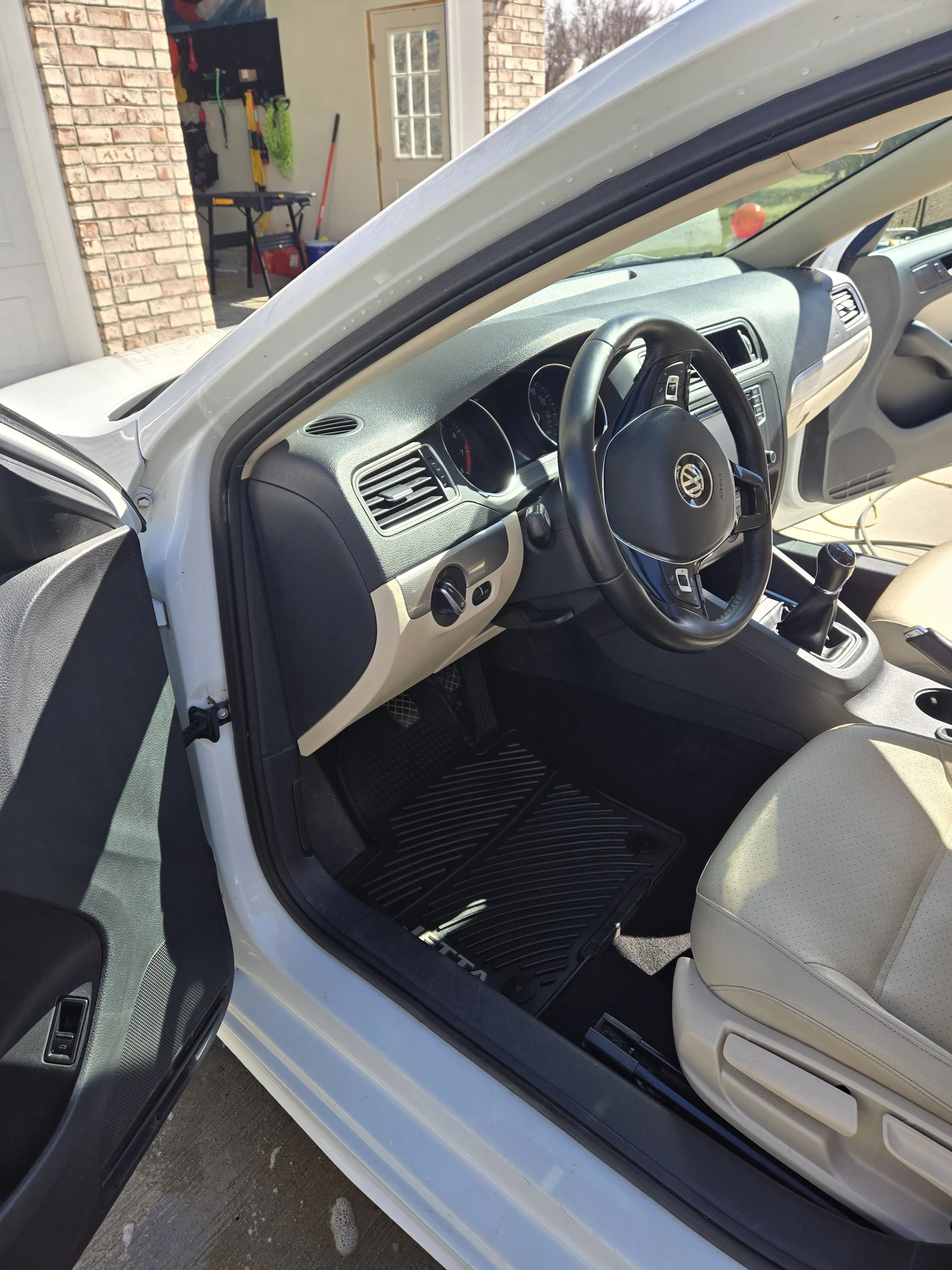 Interior view of a white Volkswagen car with the driver's side door open, showing the dashboard, steering wheel, gear shift, and beige seat.