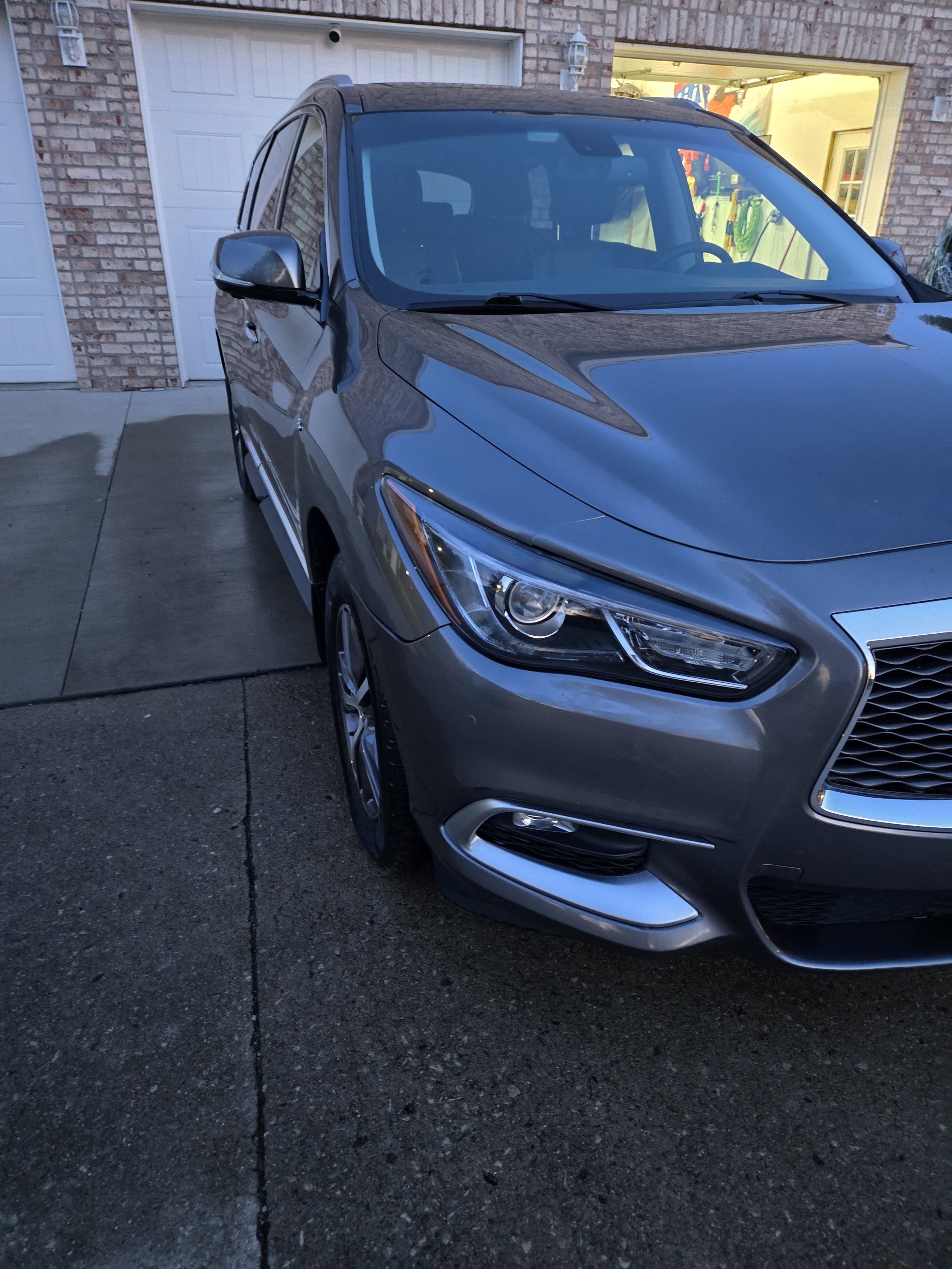 Gray sedan parked in front of a brick house with a garage door and a window with a view into the interior.