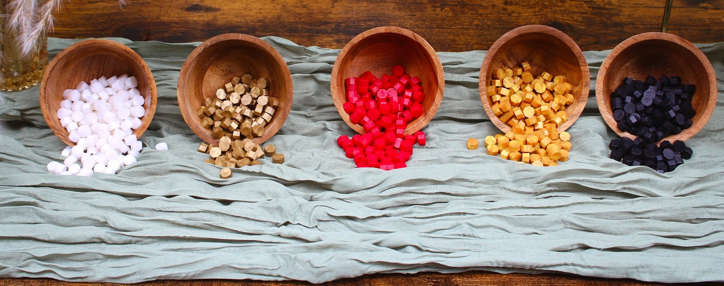 Five wooden bowls filled with colorful game pieces arranged on a light cloth surface.