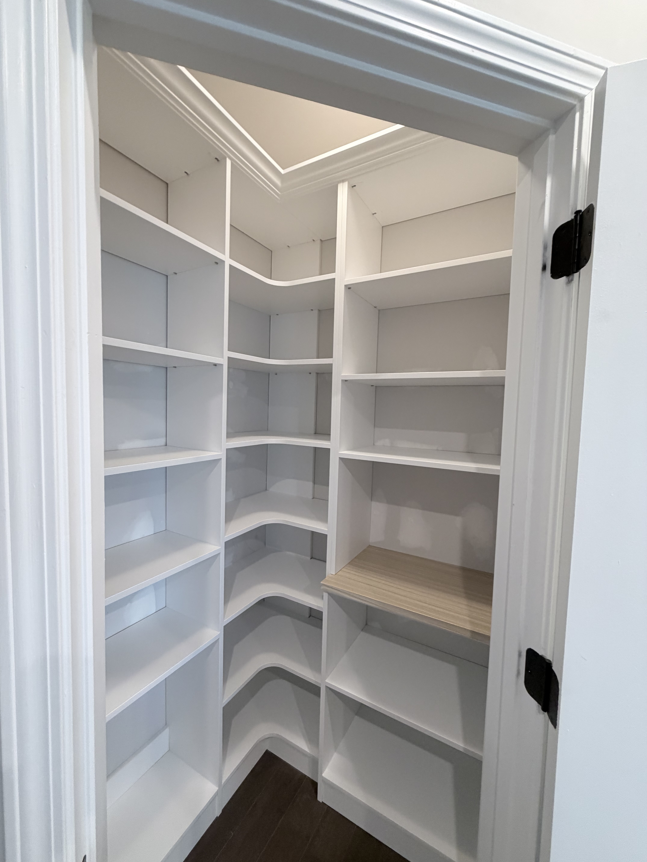 Custom white pantry with multiple shelves and a corner section, some shelves have curved edges, with a wood textured shelf in the middle.