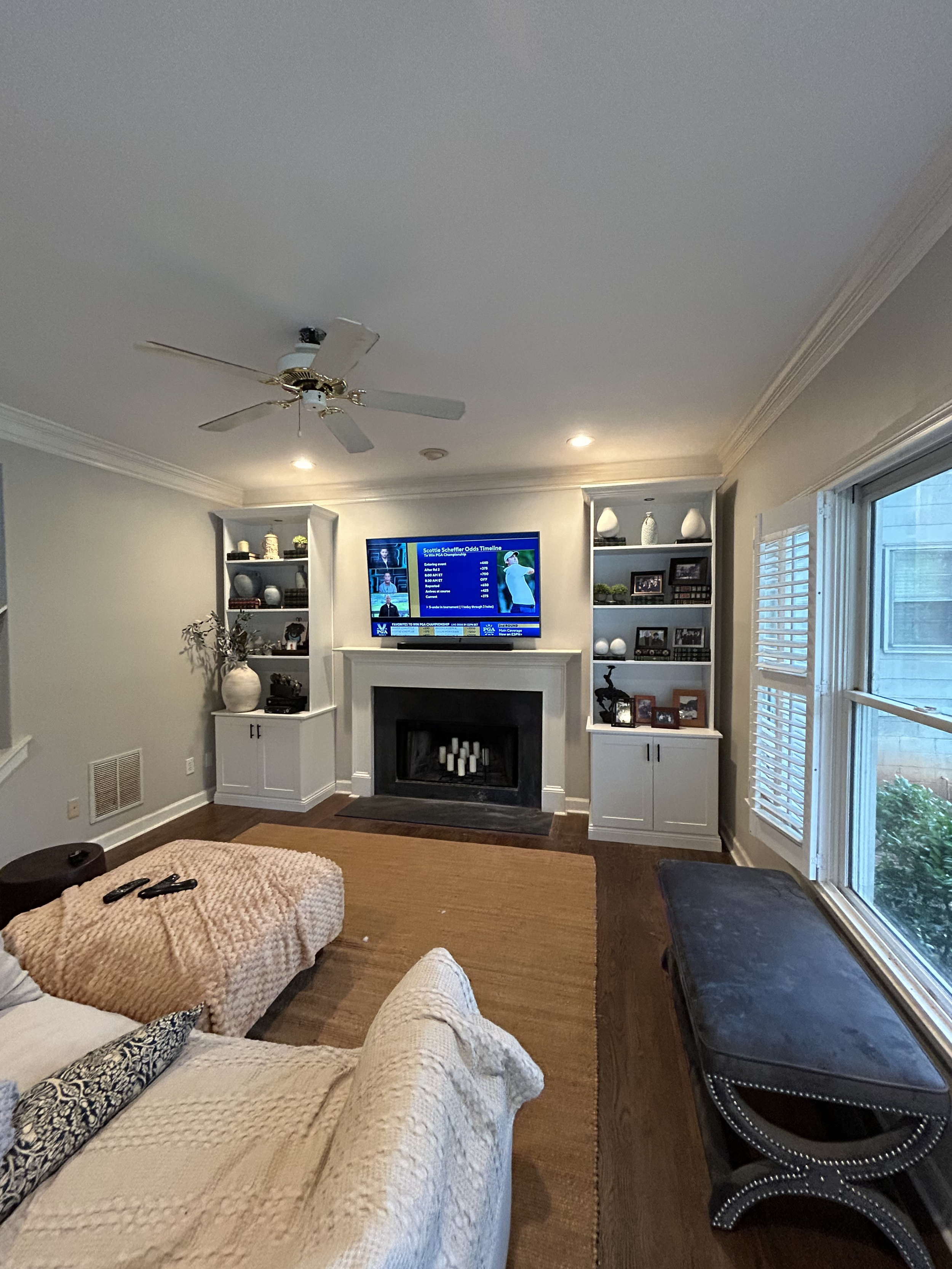 Living room with a flat-screen TV above a fireplace, with custom white built-in bookshelves on either side