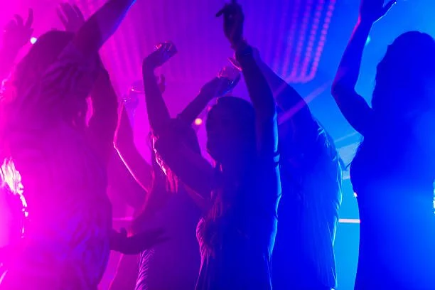 People dancing at a party with colorful purple and blue lighting.