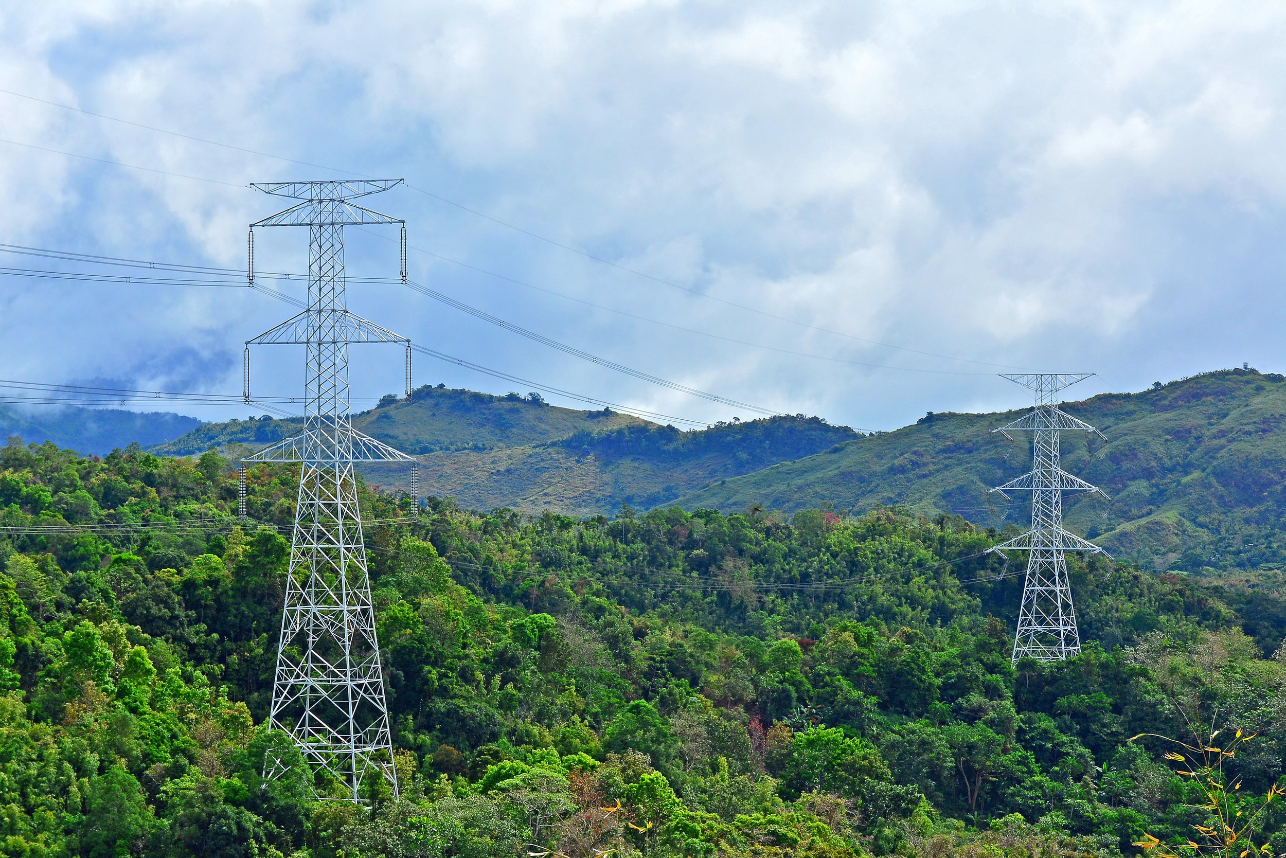 Electric power lines and towers on green hills with a cloudy blue sky.