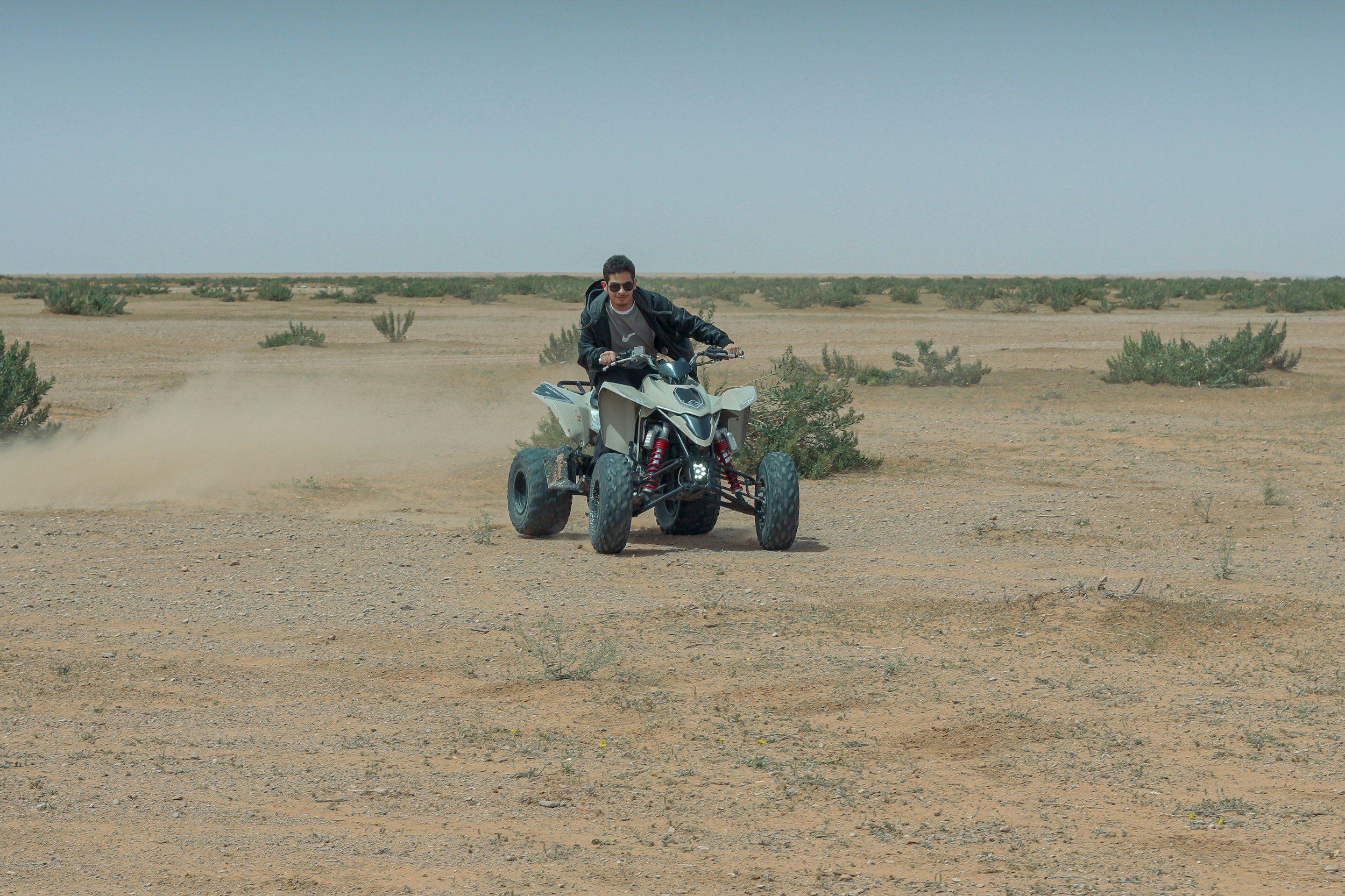 Person riding an all-terrain vehicle across a desert landscape with sparse bushes, under a cloudy sky.