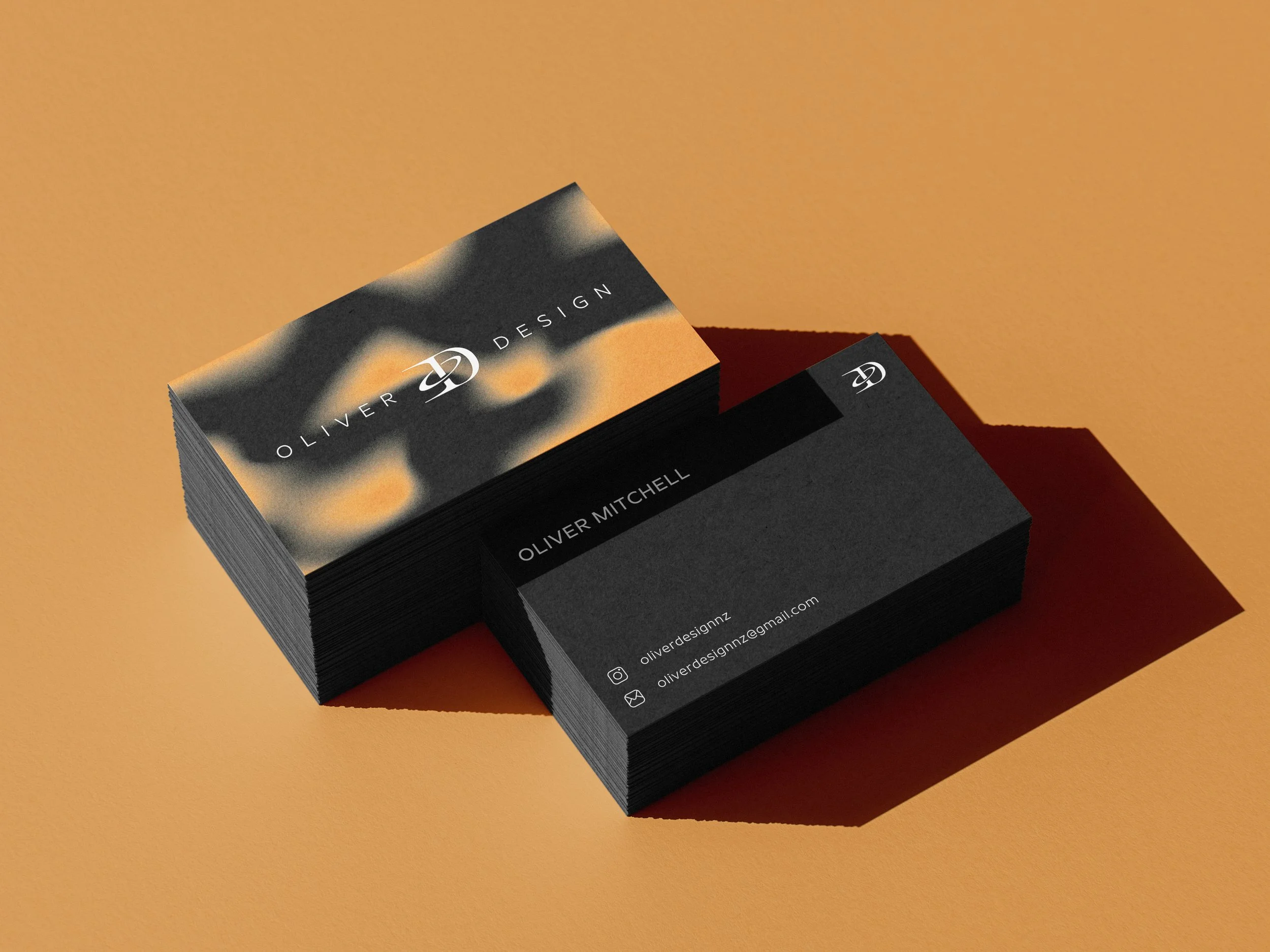 Stack of business cards for Oliver Design with a black and orange abstract background on the top card, placed on a peach-colored surface.