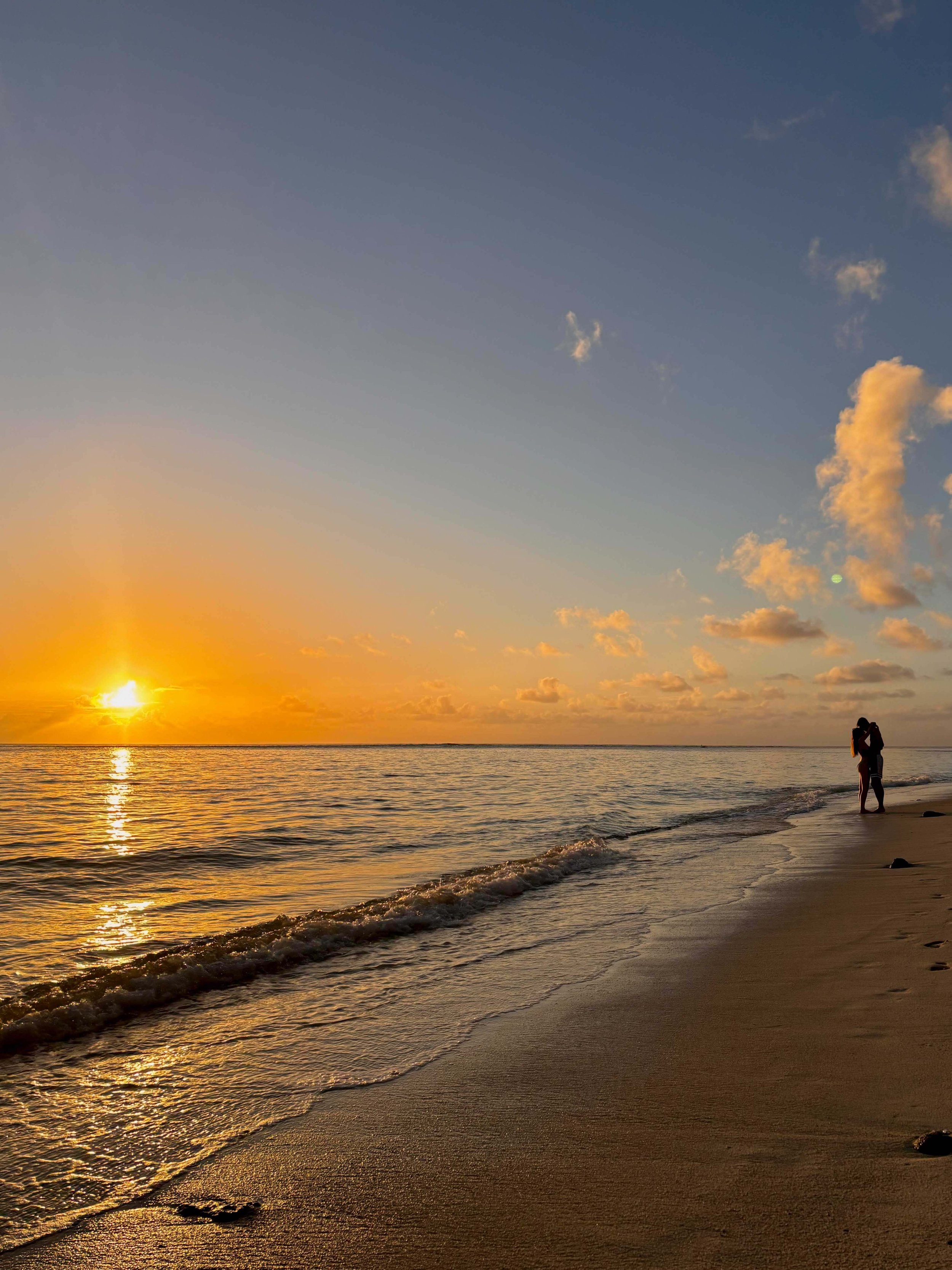 Sunset over the ocean with a couple standing on the beach.