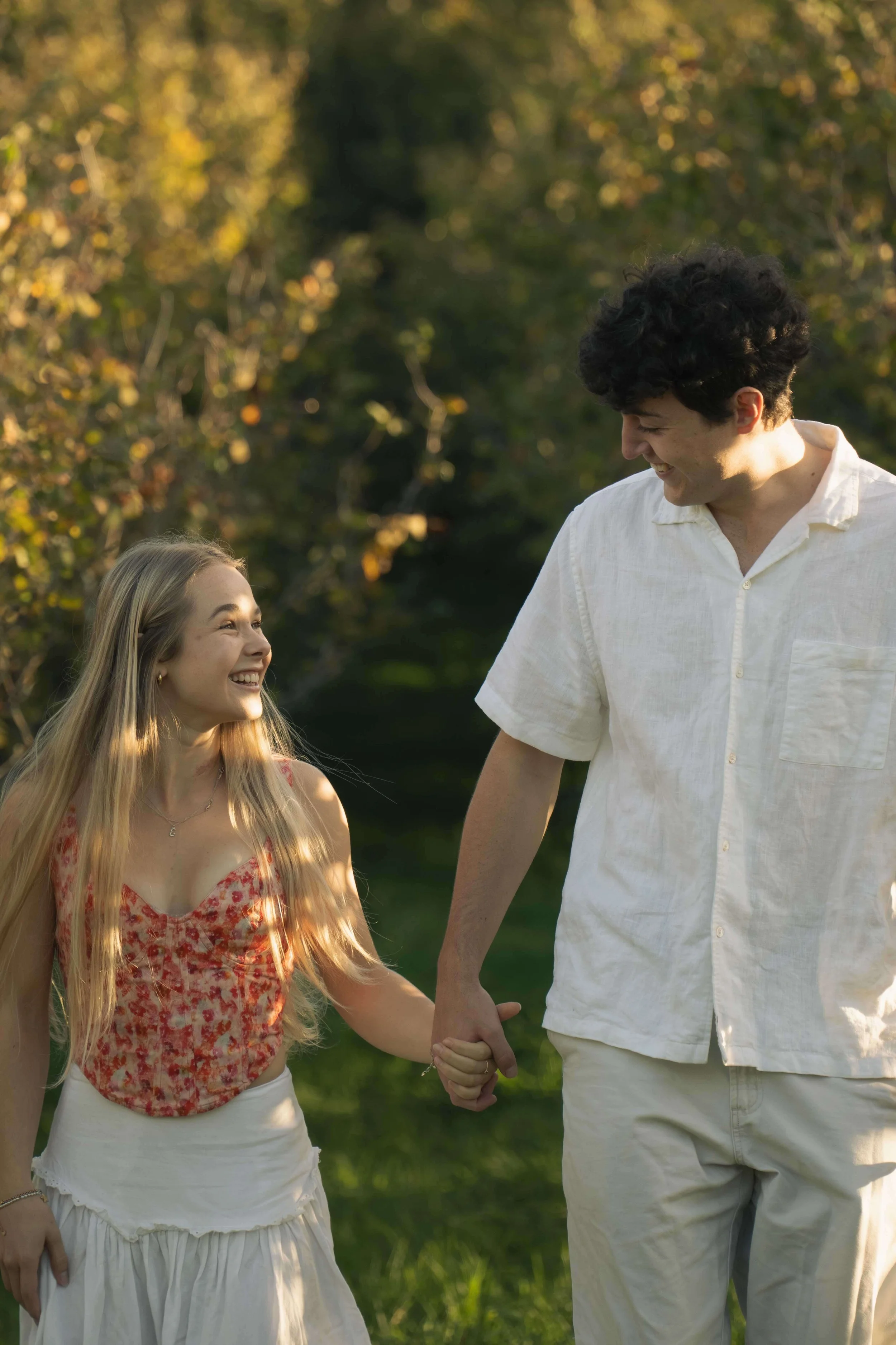 A young woman and a man holding hands and smiling at each other outdoors in a park.