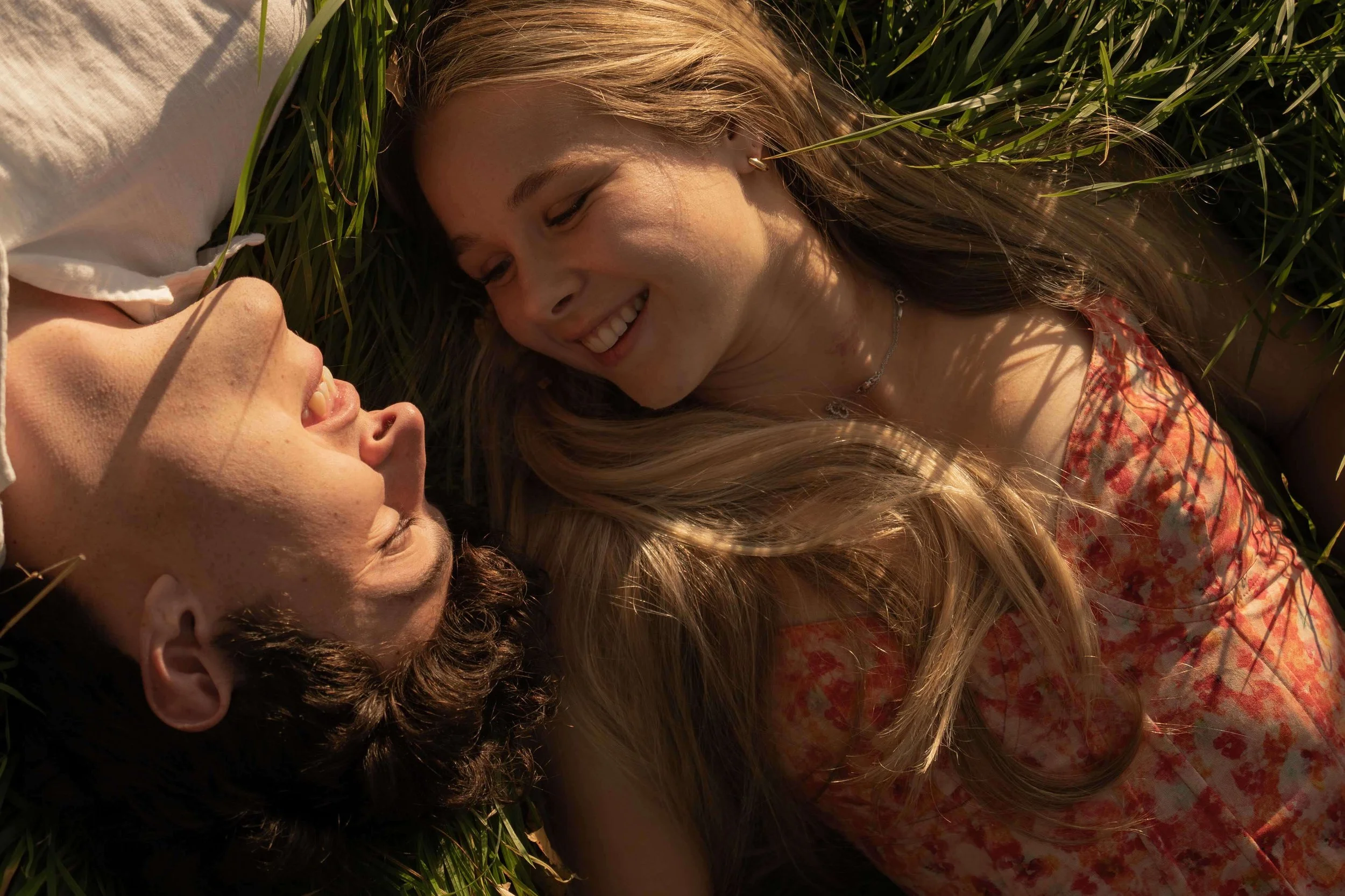 Couple lying on grass, facing each other, smiling and sharing an moment.