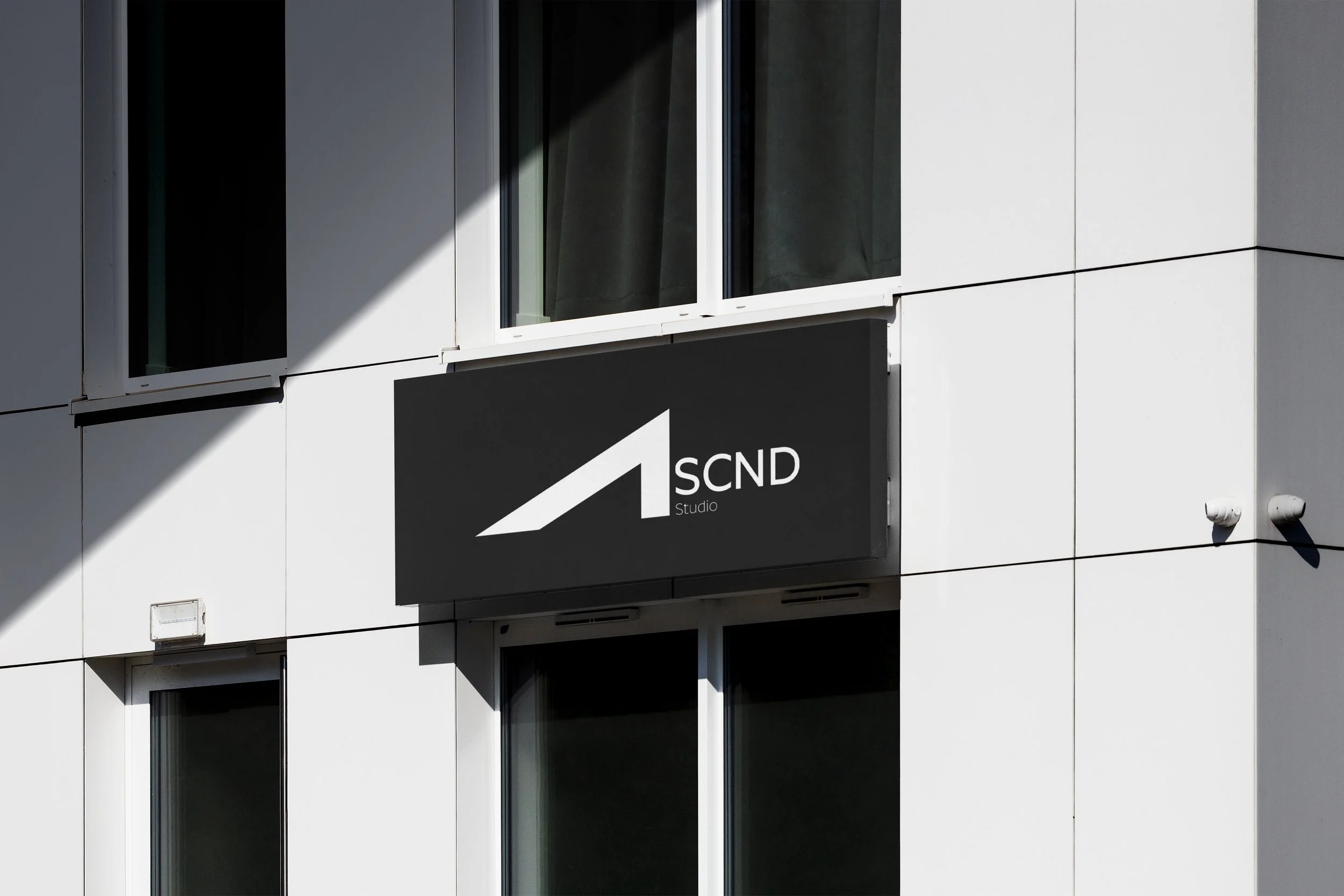 A modern building with white exterior panels and rectangular windows, featuring a black sign with a white stylized arrow and the text 'SCND Studio'.