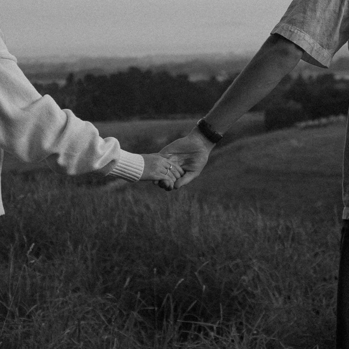 Two people holding hands outdoors in a grassy field, black and white photo.