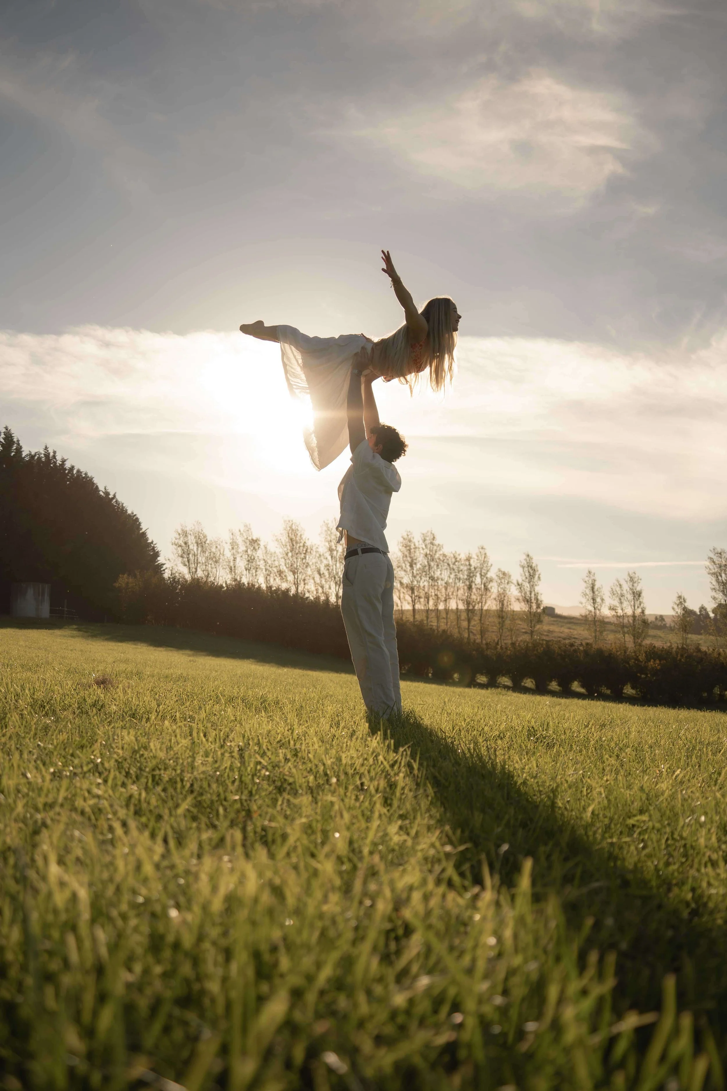 A person holding another person in a pose outdoors with the sun setting behind them.