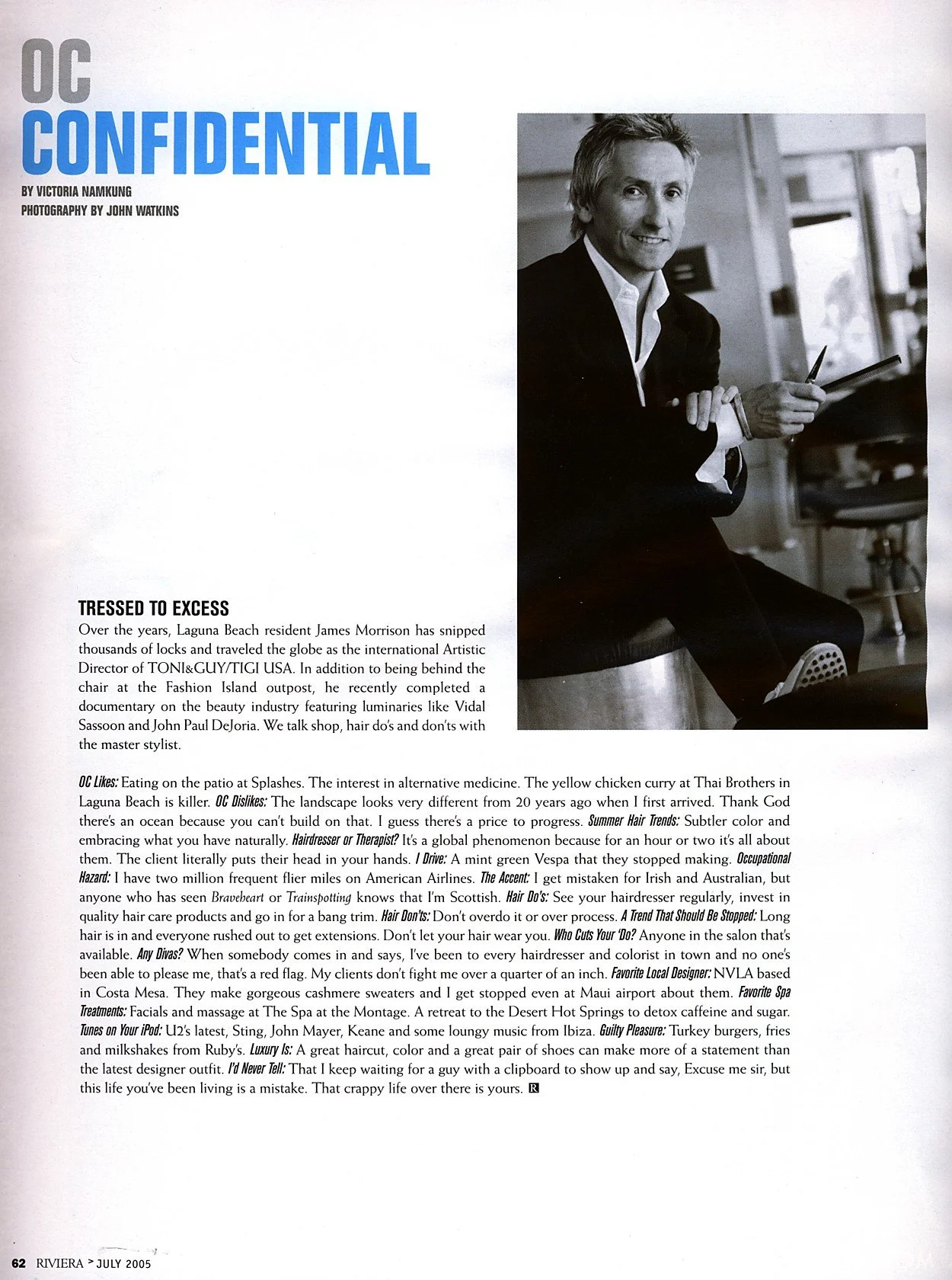 A black-and-white photograph of a smiling man with blond hair, wearing a dark suit and white shirt, sitting indoors and holding a tablet and stylus.