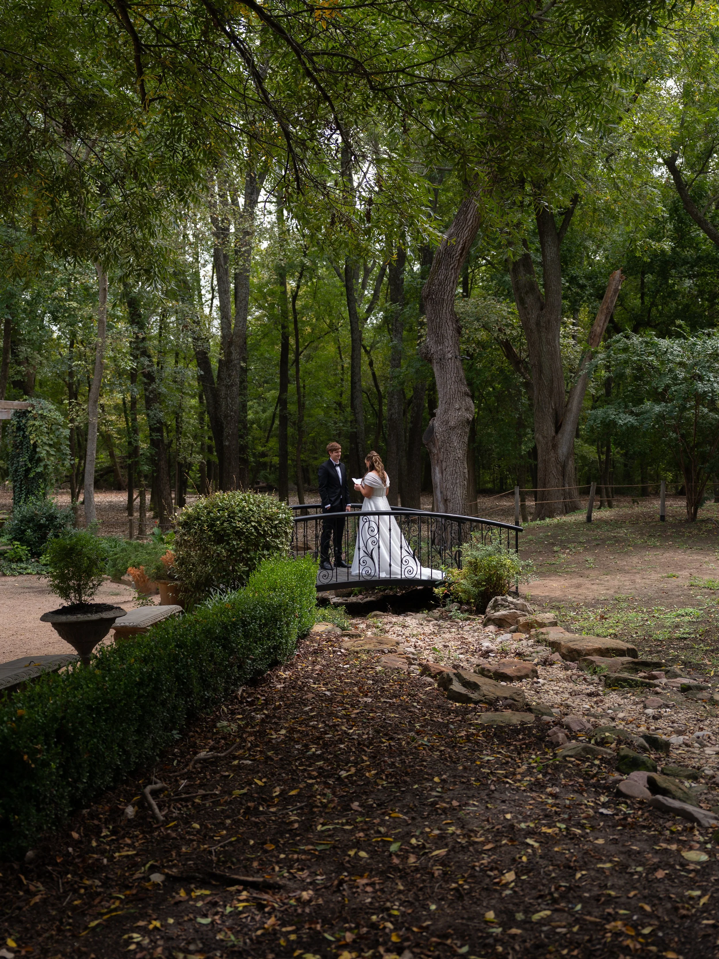 A scenic portrait during first look and private vows in Waxahachie, Texas, capturing the couple on a small bridge surrounded by lush greenery.