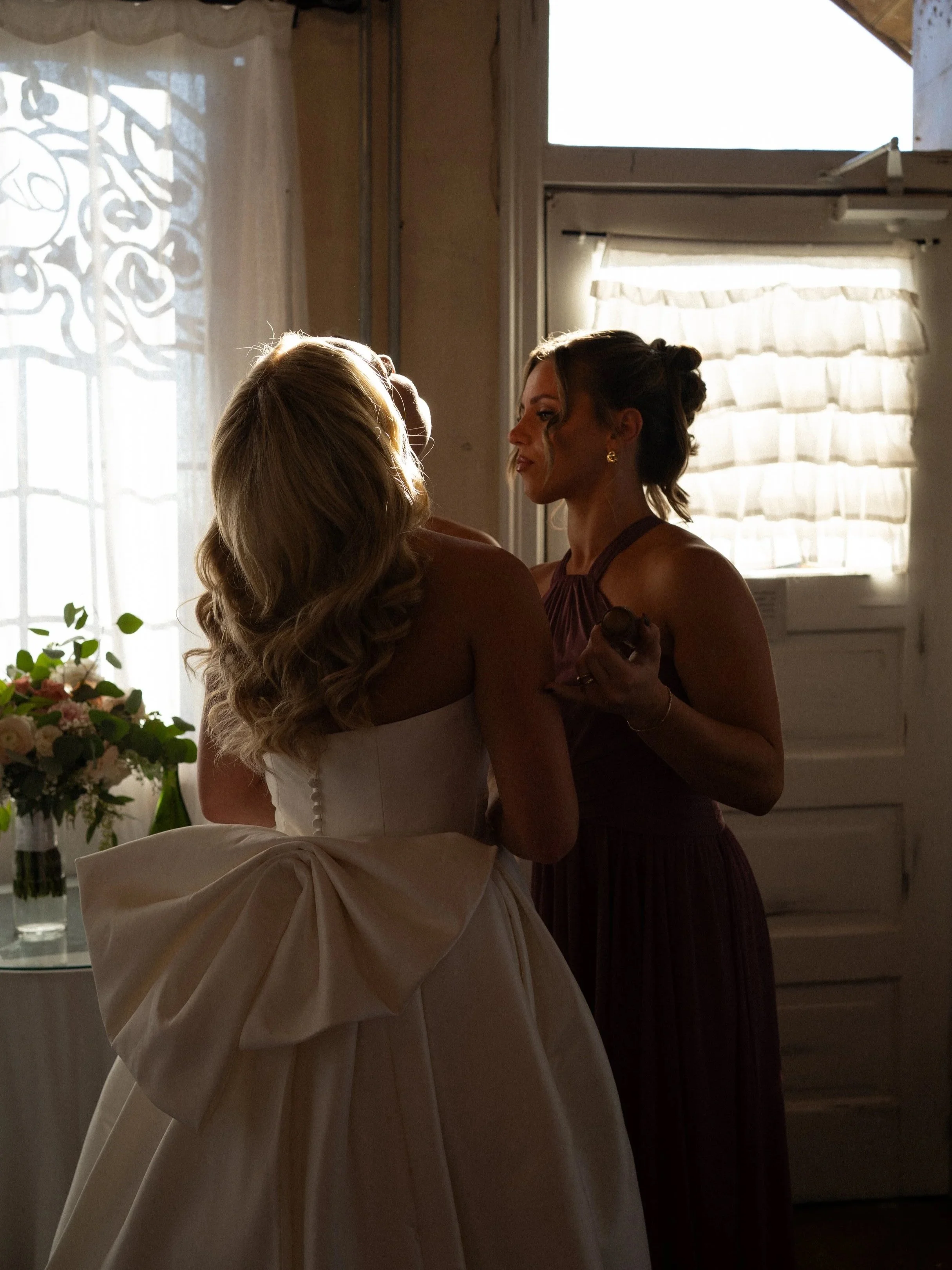 Soft morning light pours through a Montgomery, Texas bridal suite as the bride shares an intimate getting-ready moment with her bridesmaid, capturing the quiet anticipation before the ceremony.