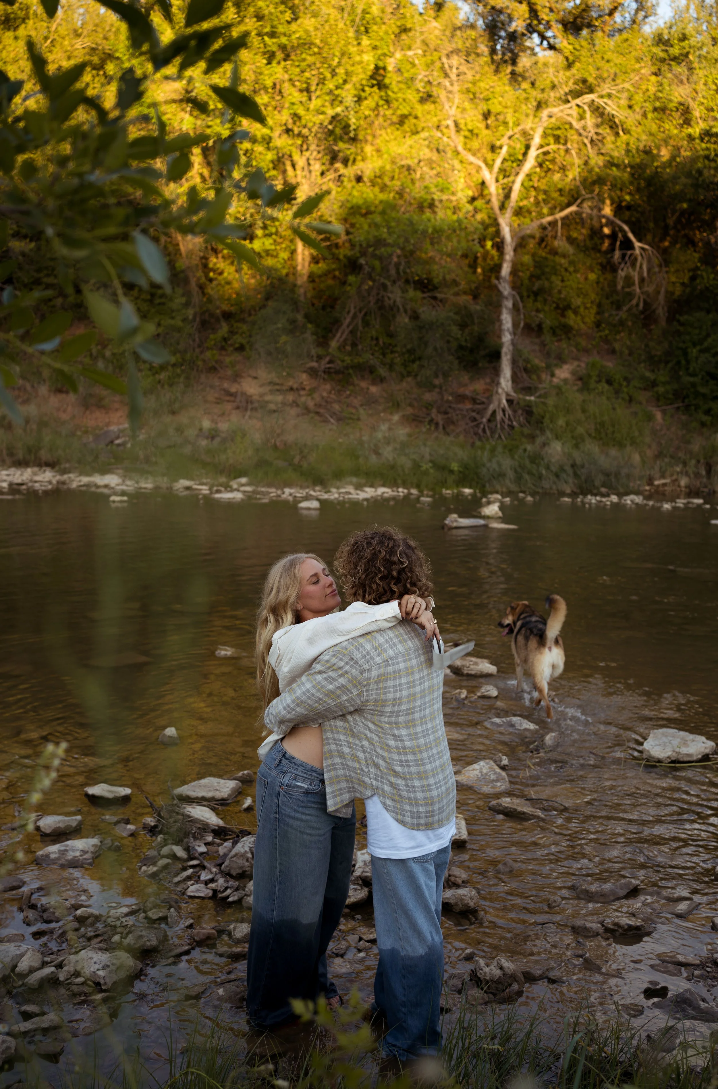 A heartfelt moment in Rainbow, Texas, as the couple embraces by the river, surrounded by nature and their dogs.