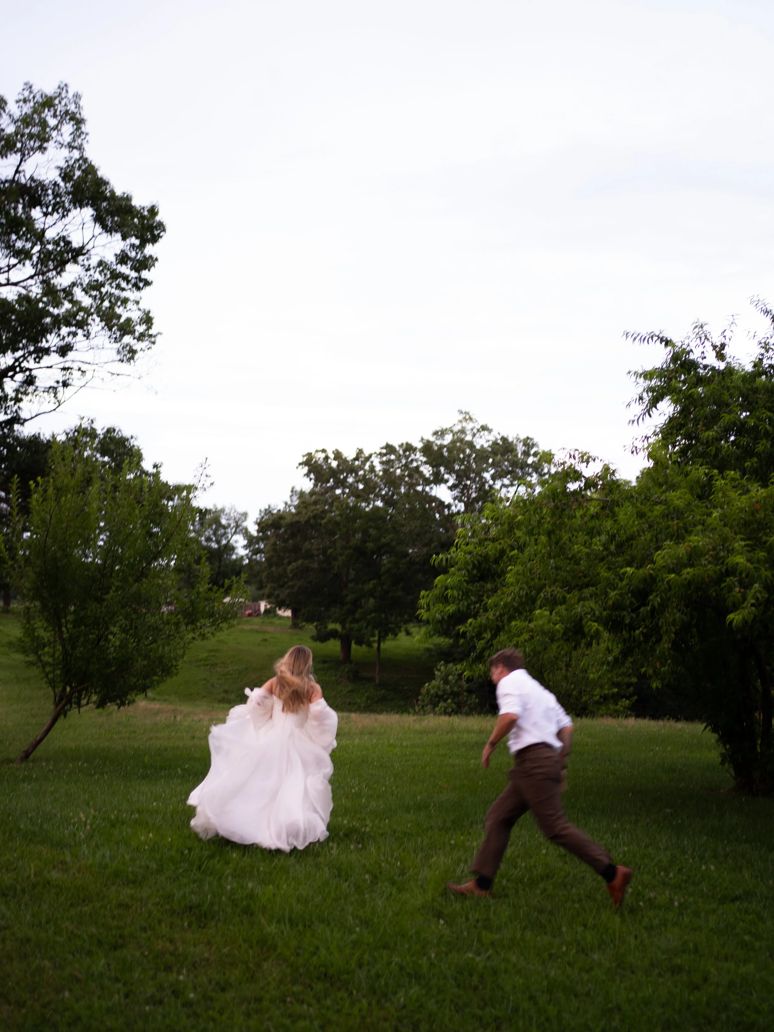 Bride and groom running through a field