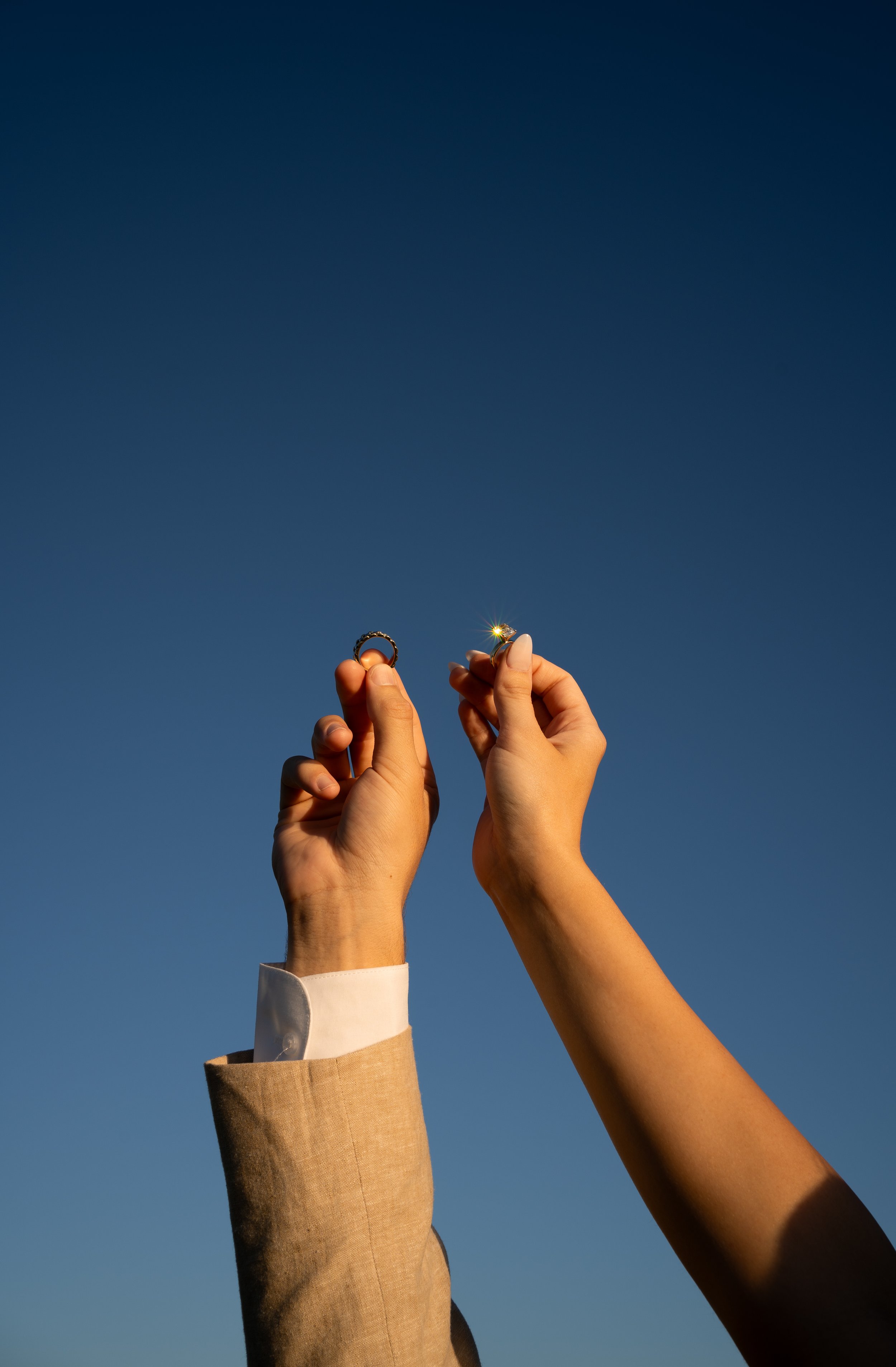 Wedding rings held in golden light against a clear blue sky during a backyard tent wedding in Fort Worth, Texas.