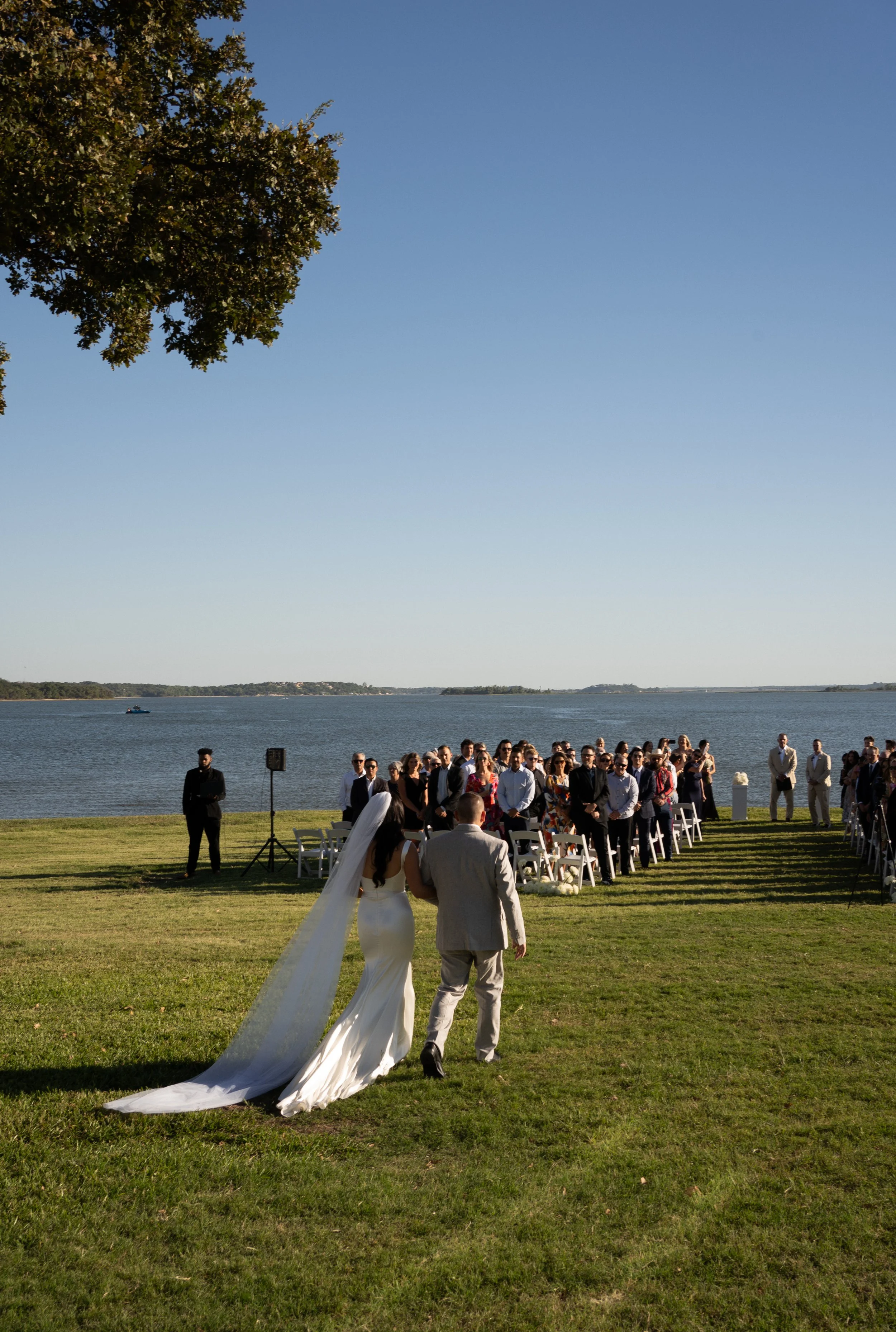 Bride walking down aisle during outdoor wedding ceremony overlooking the water during a backyard tent wedding in Fort Worth, Texas.