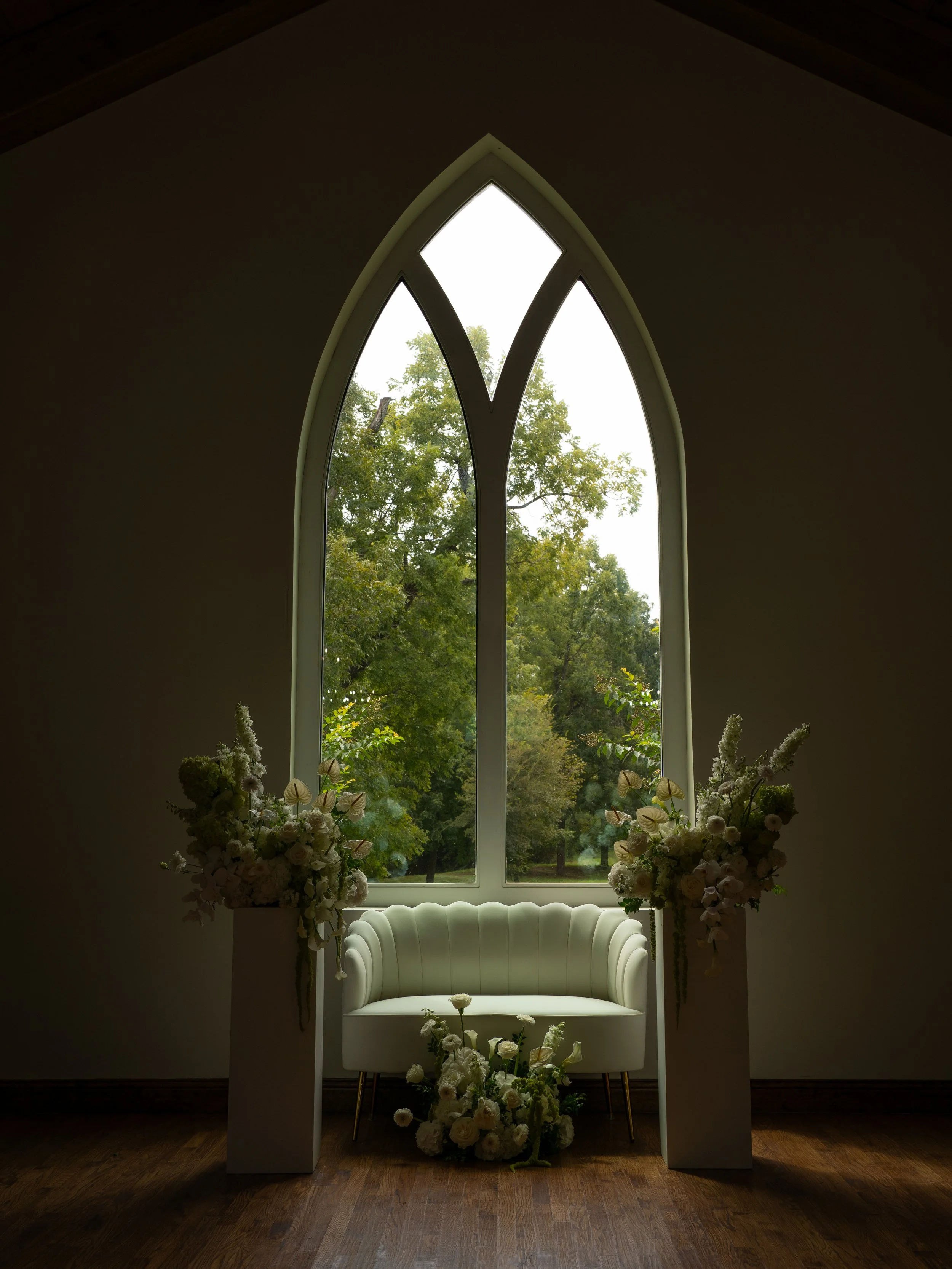 A quiet ceremony detail in Waxahachie, TX, featuring an arched window and soft floral arrangements before guests are seated.
