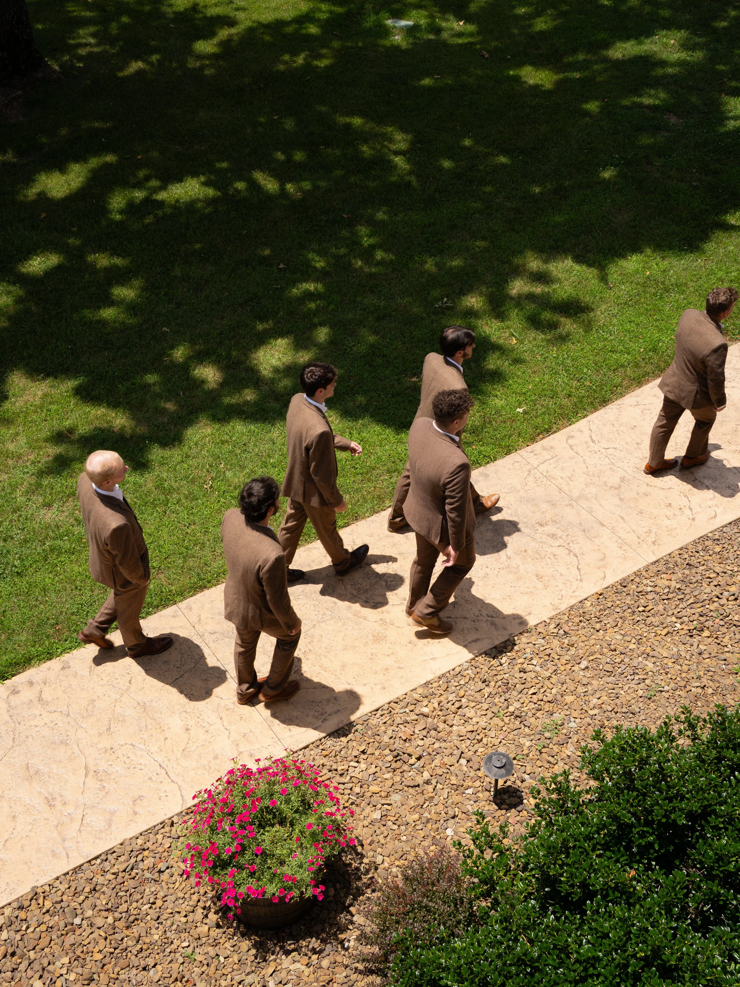 Groom and groomsmen walking along garden path at wedding venue