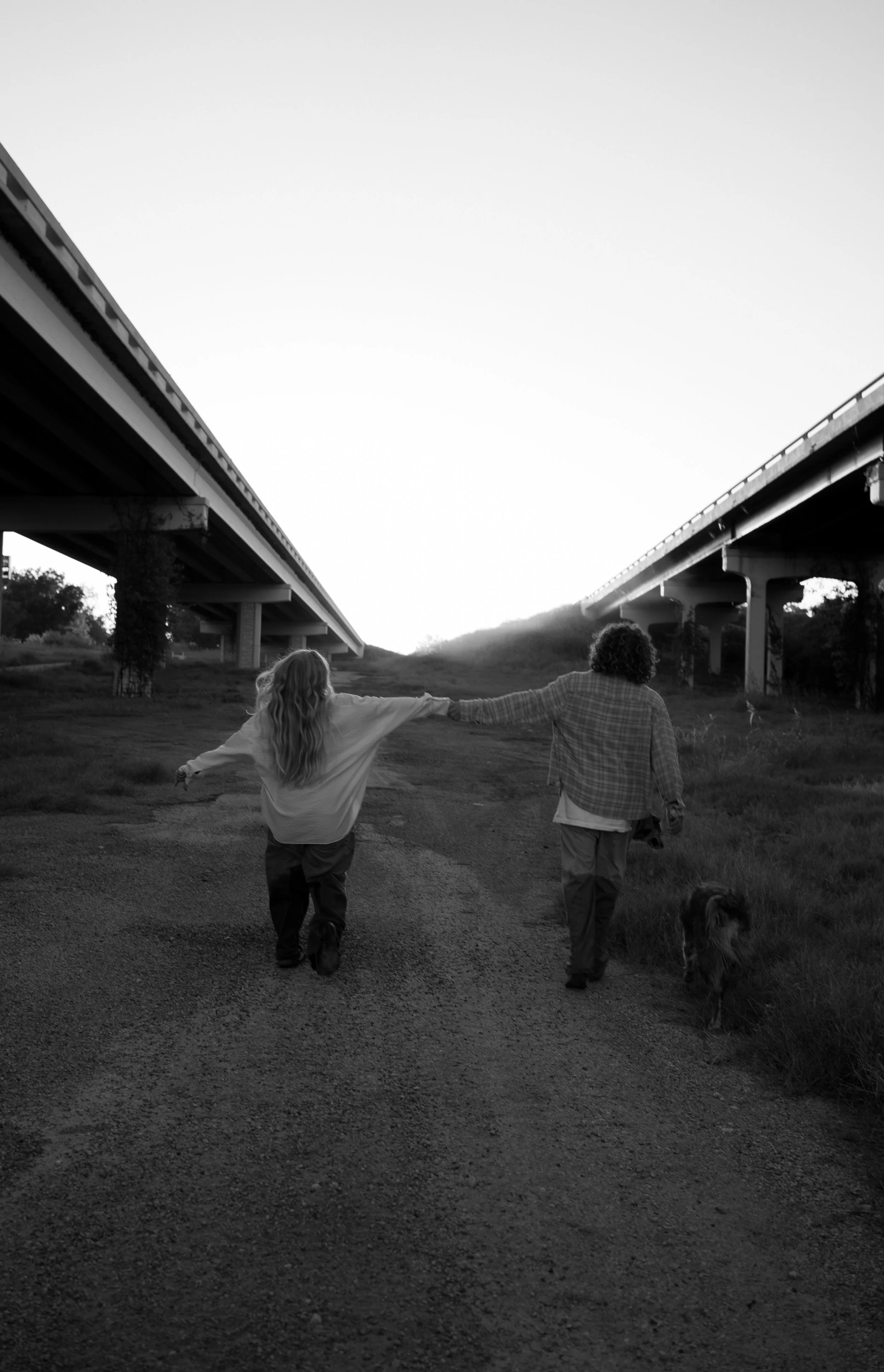 A wide, black-and-white storytelling moment in Rainbow, TX, capturing the couple walking together beneath an open sky.