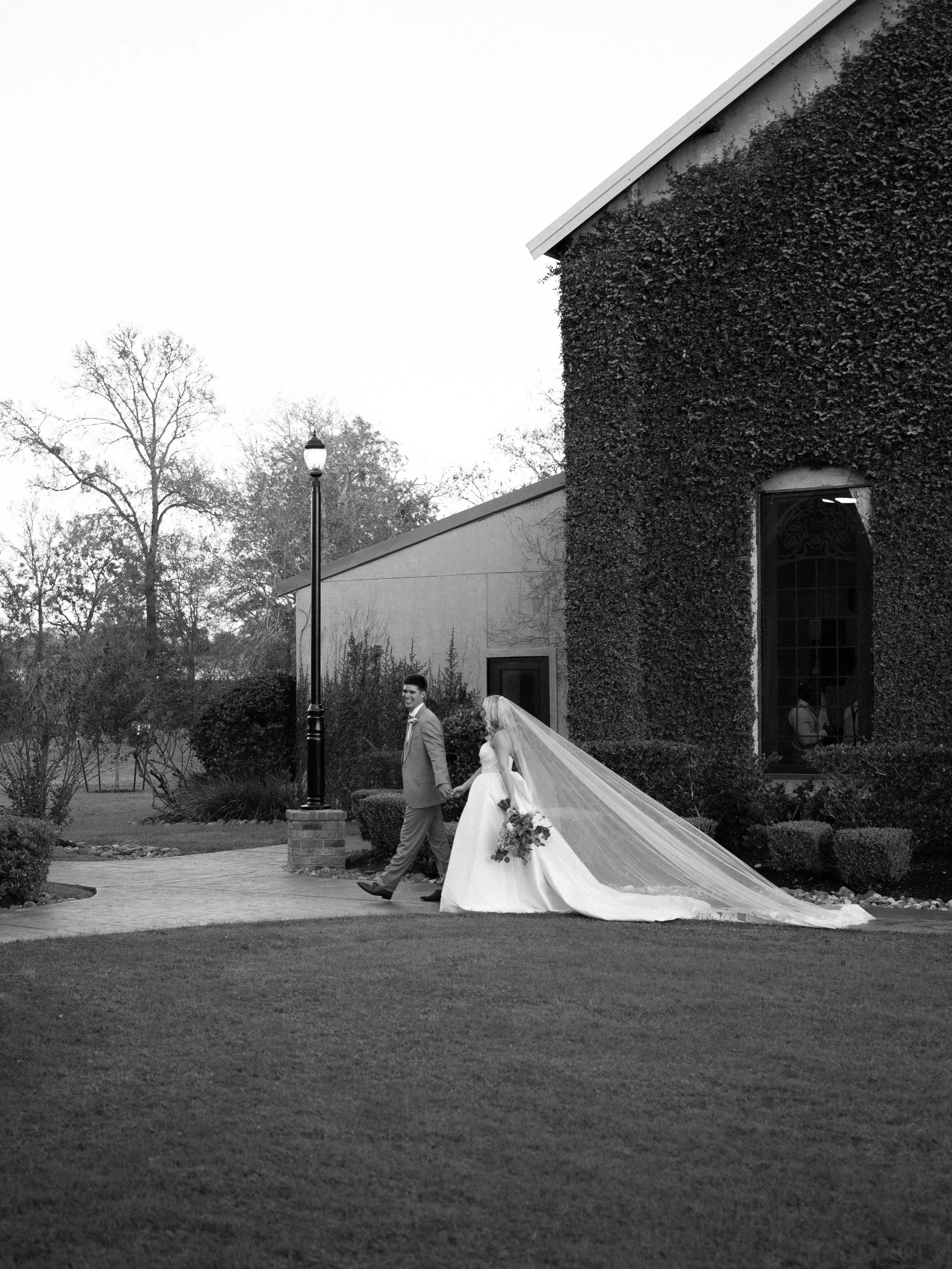 wide, documentary-style black-and-white image of the couple exiting their ceremony in Montgomery, Texas, surrounded by architecture and open space.