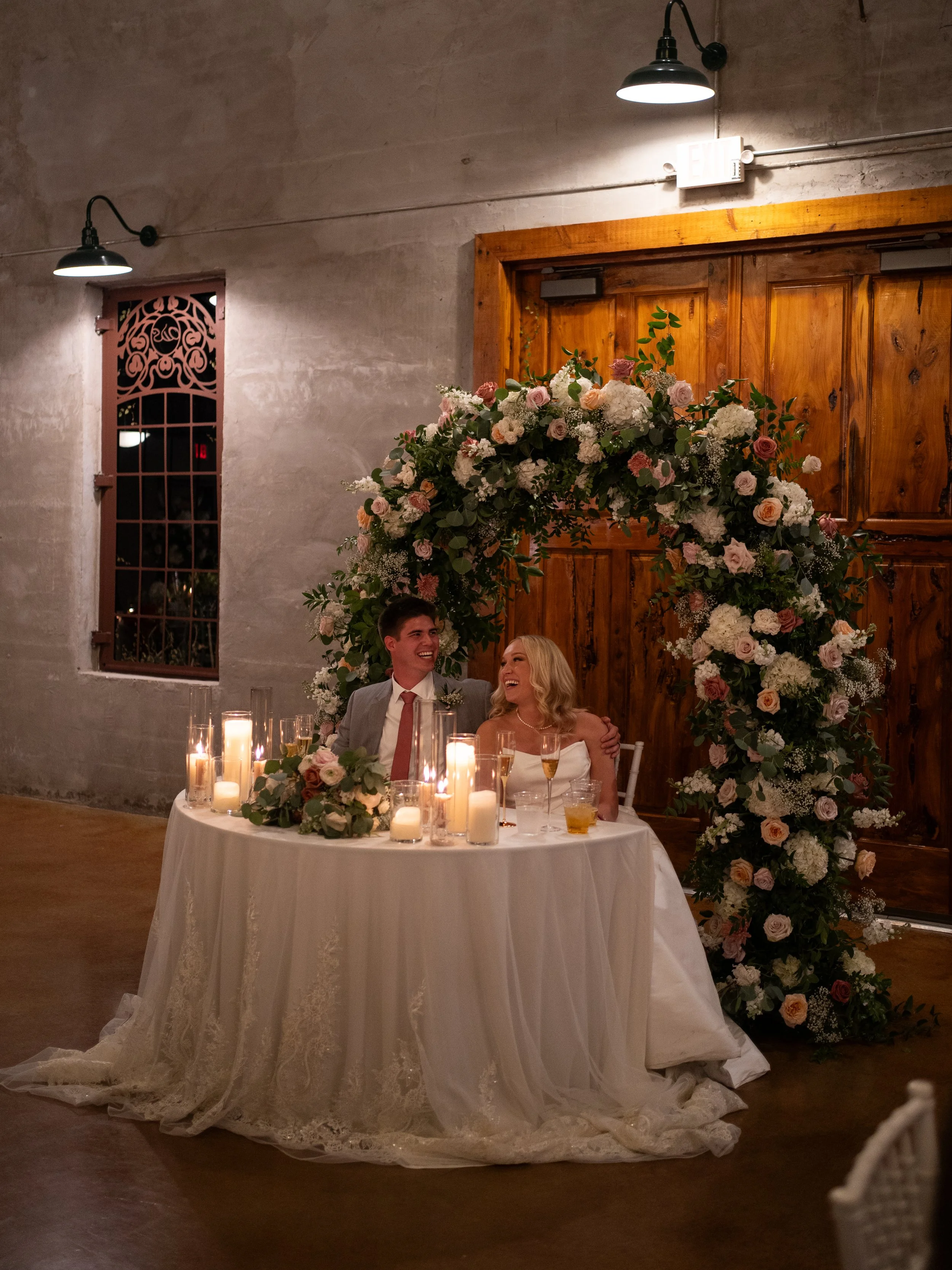 A beautifully styled reception table in Montgomery, Texas, featuring soft florals and candlelight-inspired ambiance for an elevated and romantic setting. Bride and groom laughing during toasts.