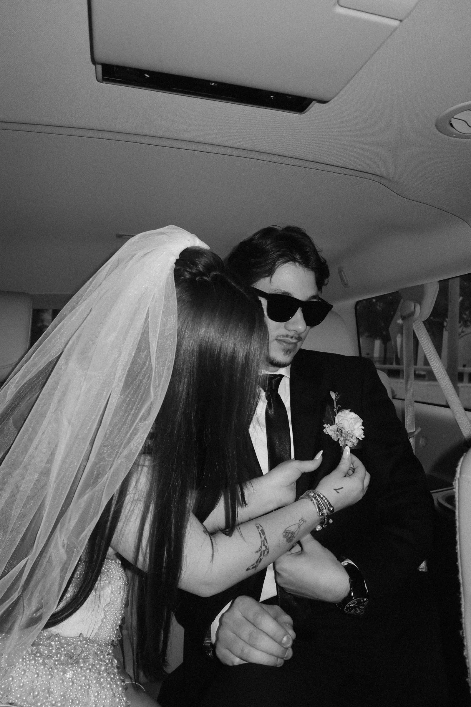 A candid black-and-white moment in Houston, Texas, as the bride pins boutonniere on the groom inside a car.