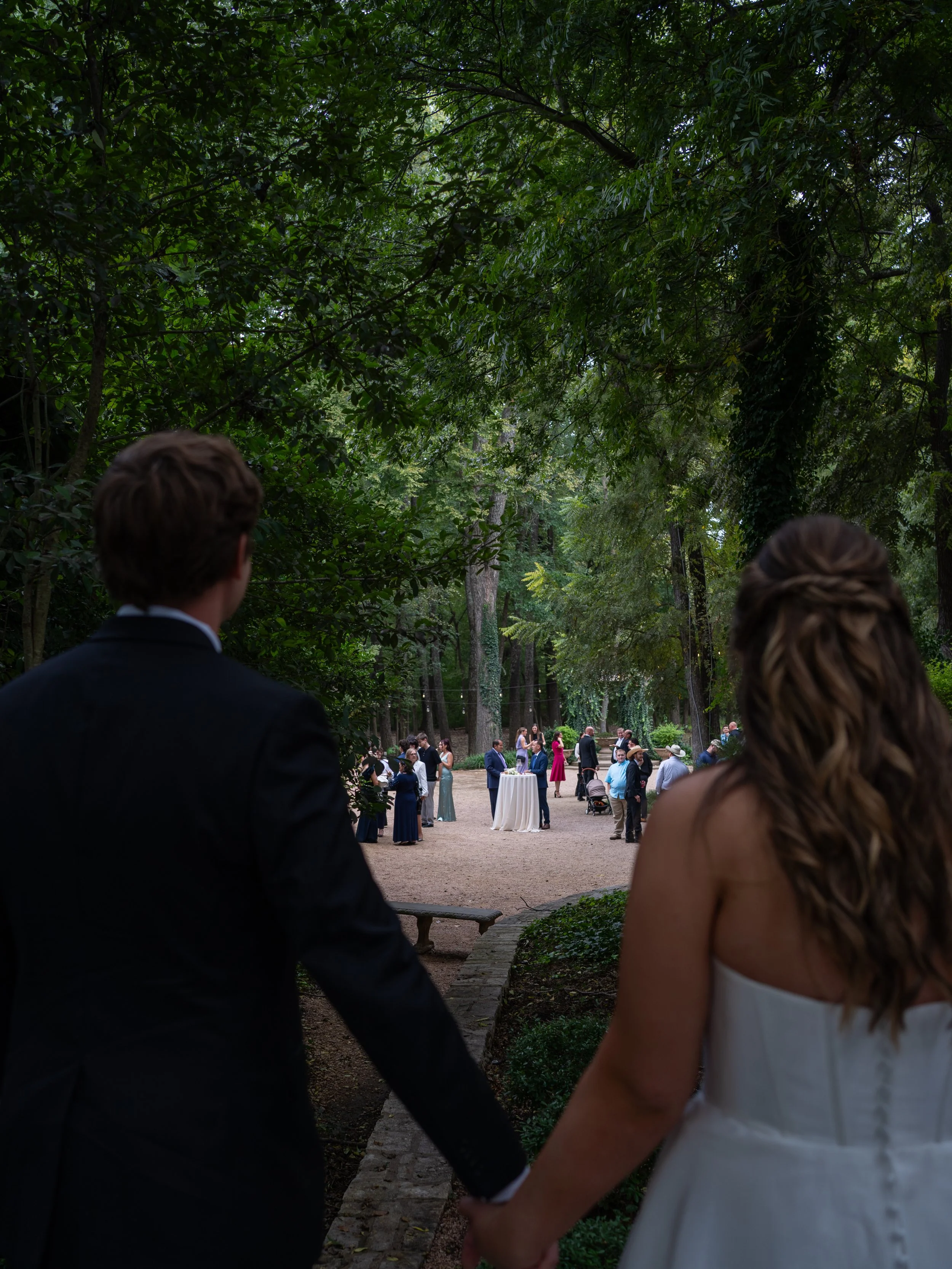 A documentary-style perspective in Waxahachie, TX, as the couple approaches their ceremony surrounded by guests and nature.