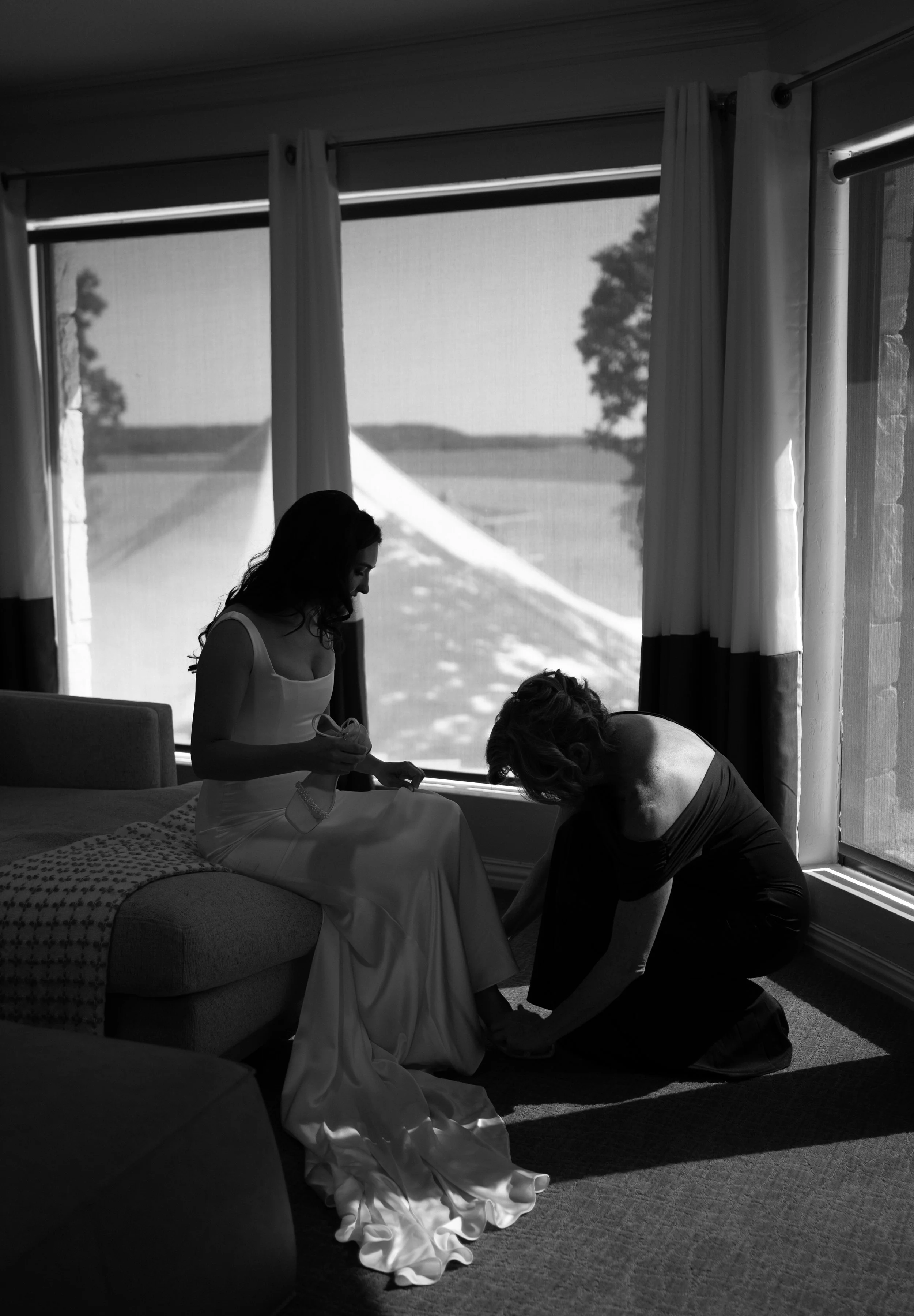 Quiet candid moment of mother of the bride putting her shoes on captured in soft window light.