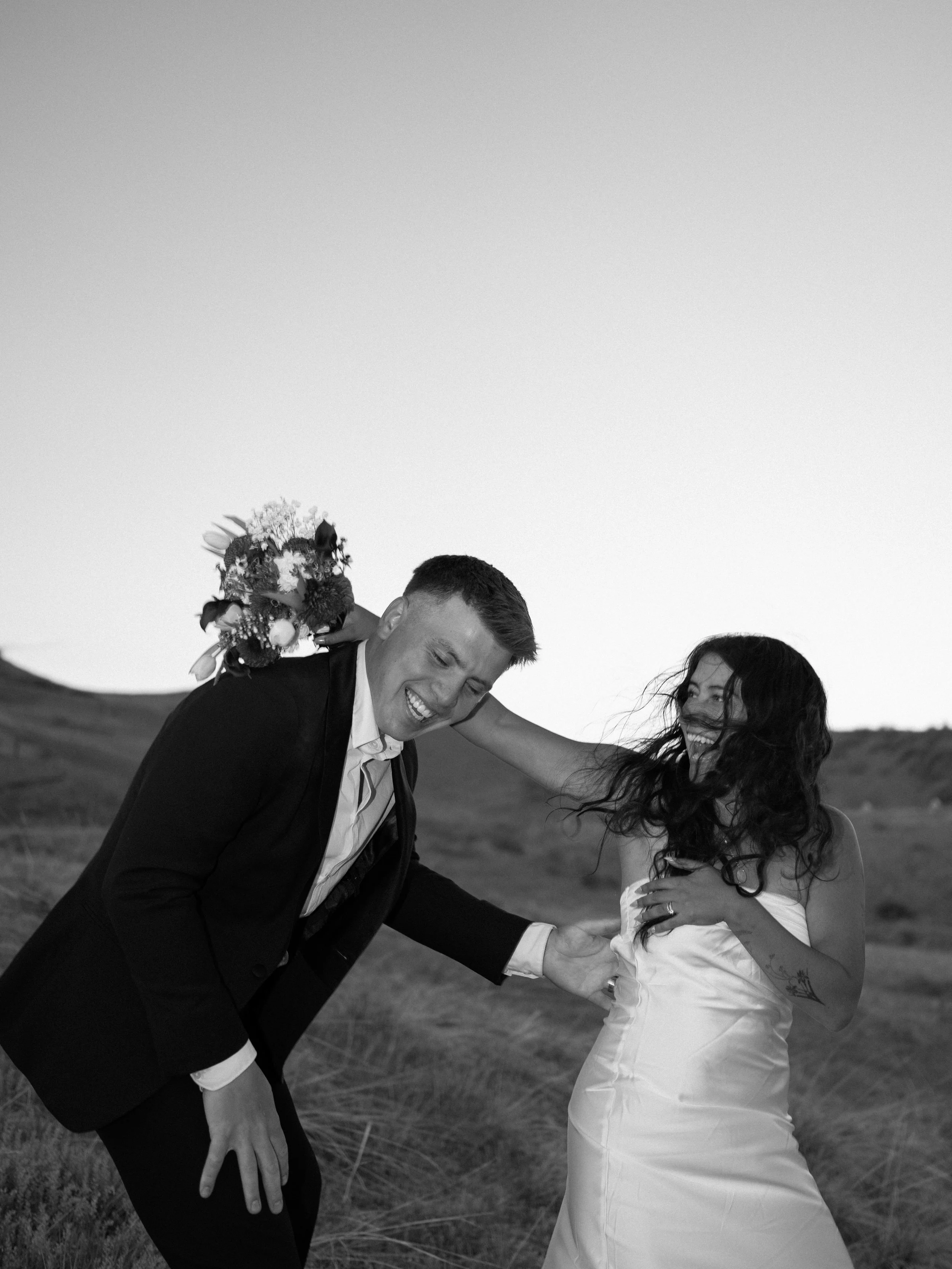 Playful black and white photo of bride and groom laughing together in the hills of Boulder Colorado during a candid wedding moment