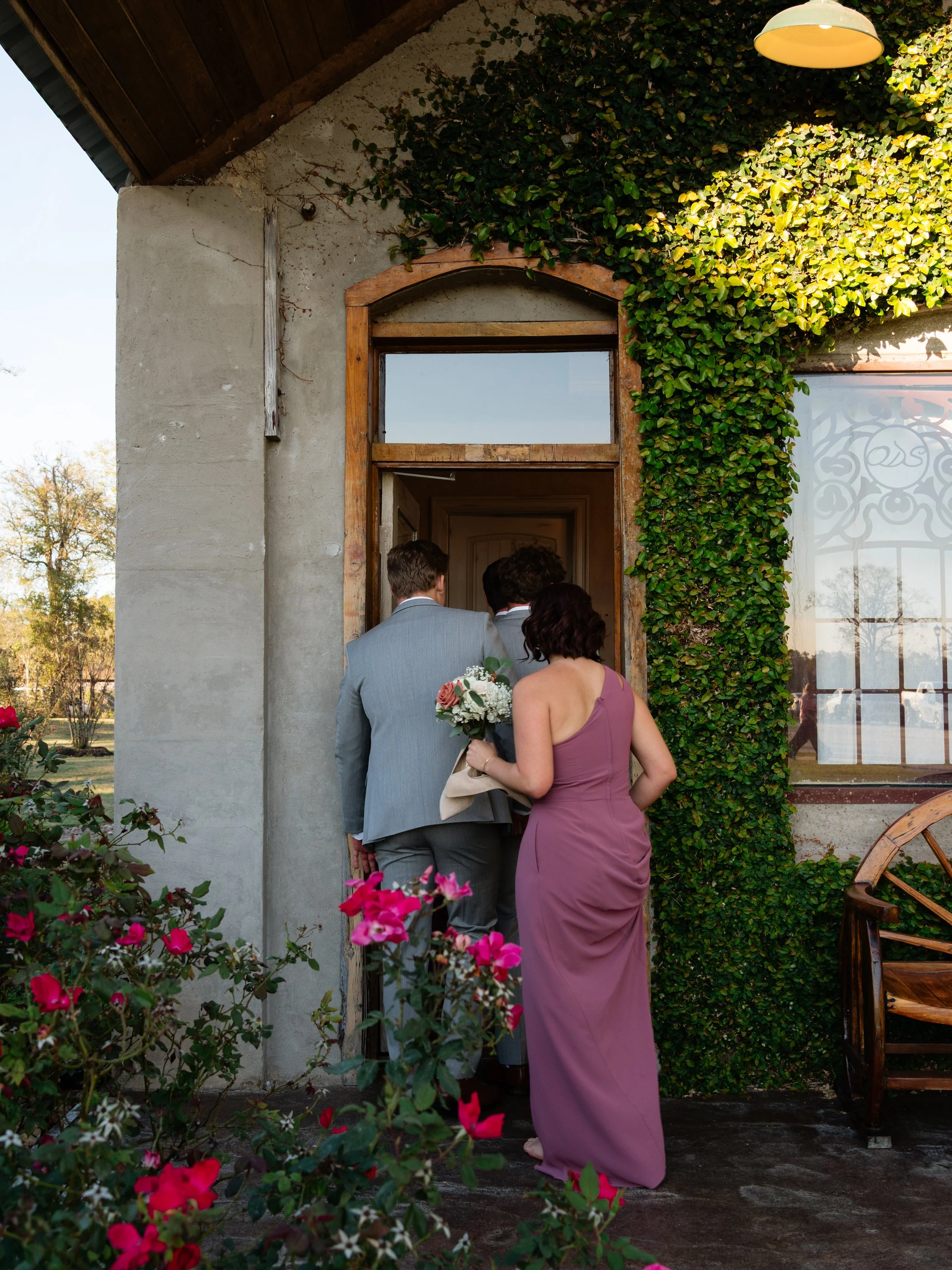 The wedding party steps into bridal suite at Montgomery, TX venue through a charming doorway framed with florals, marking a quiet and meaningful transition in their day.