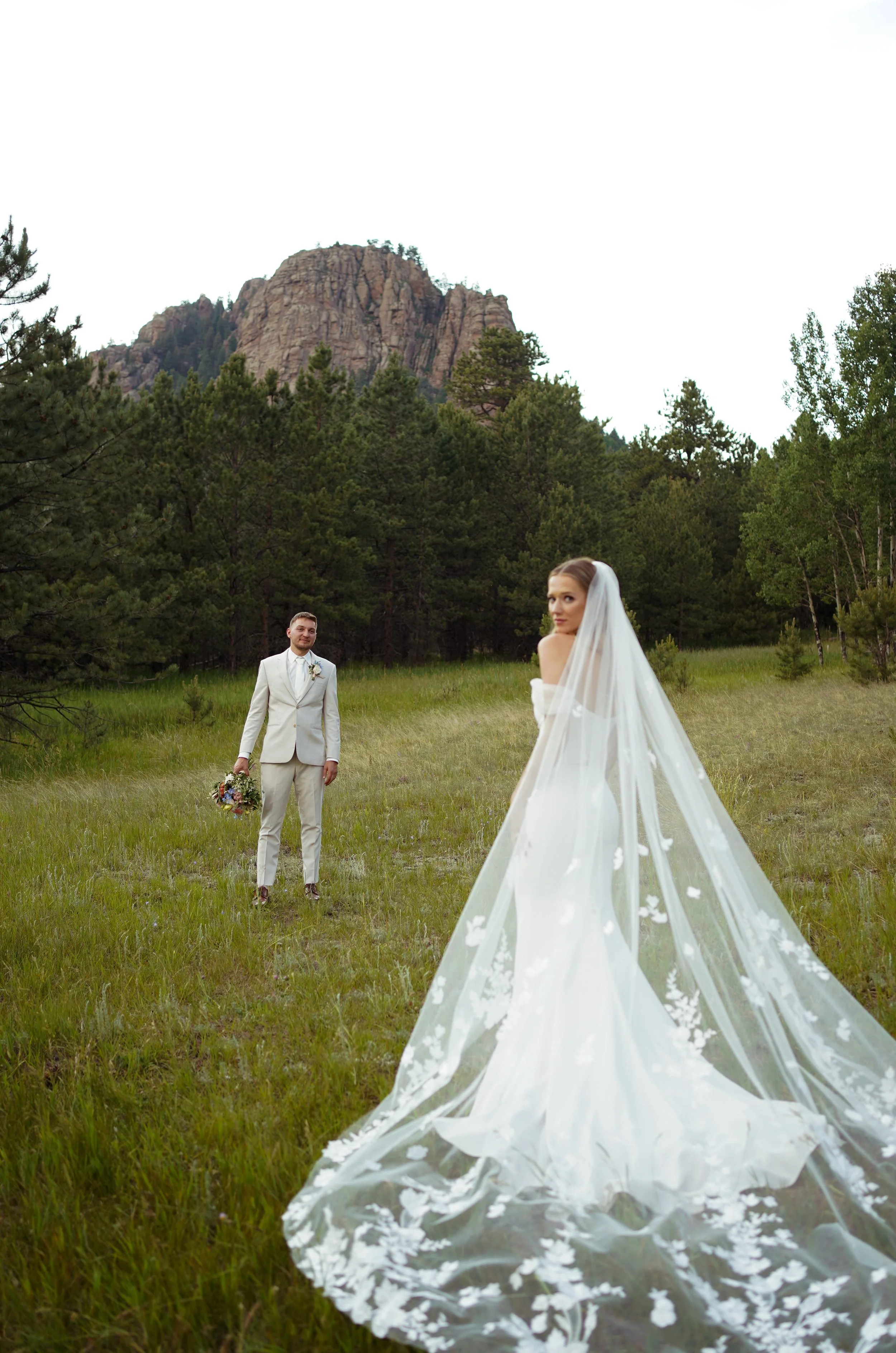 Bride walking through a field with a long flowing veil during a romantic Pine, Colorado wedding.