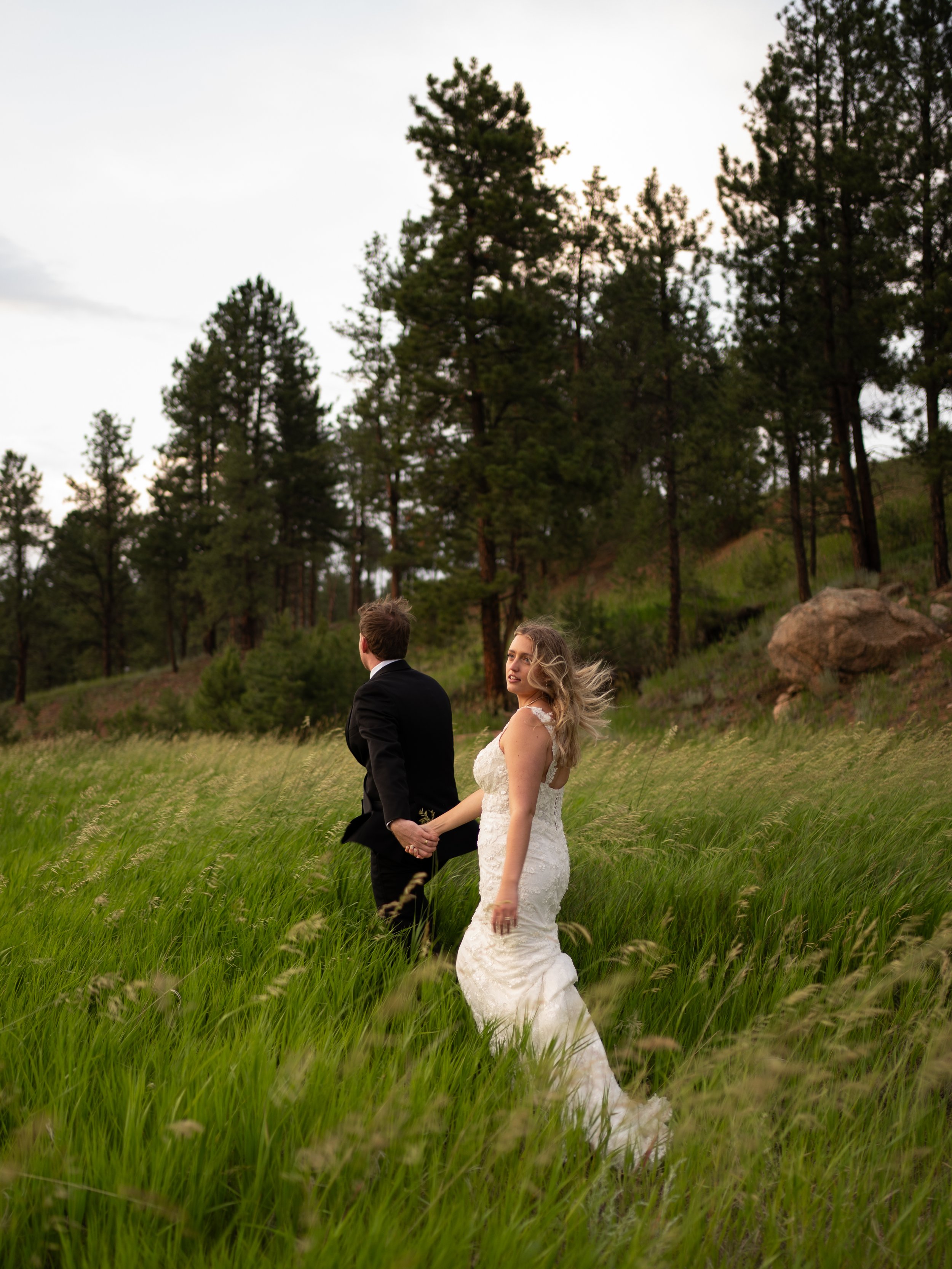 Bride and groom walking hand in hand through a grassy field at Pikes Peak Ranch in Woodland Park Colorado with mountain views