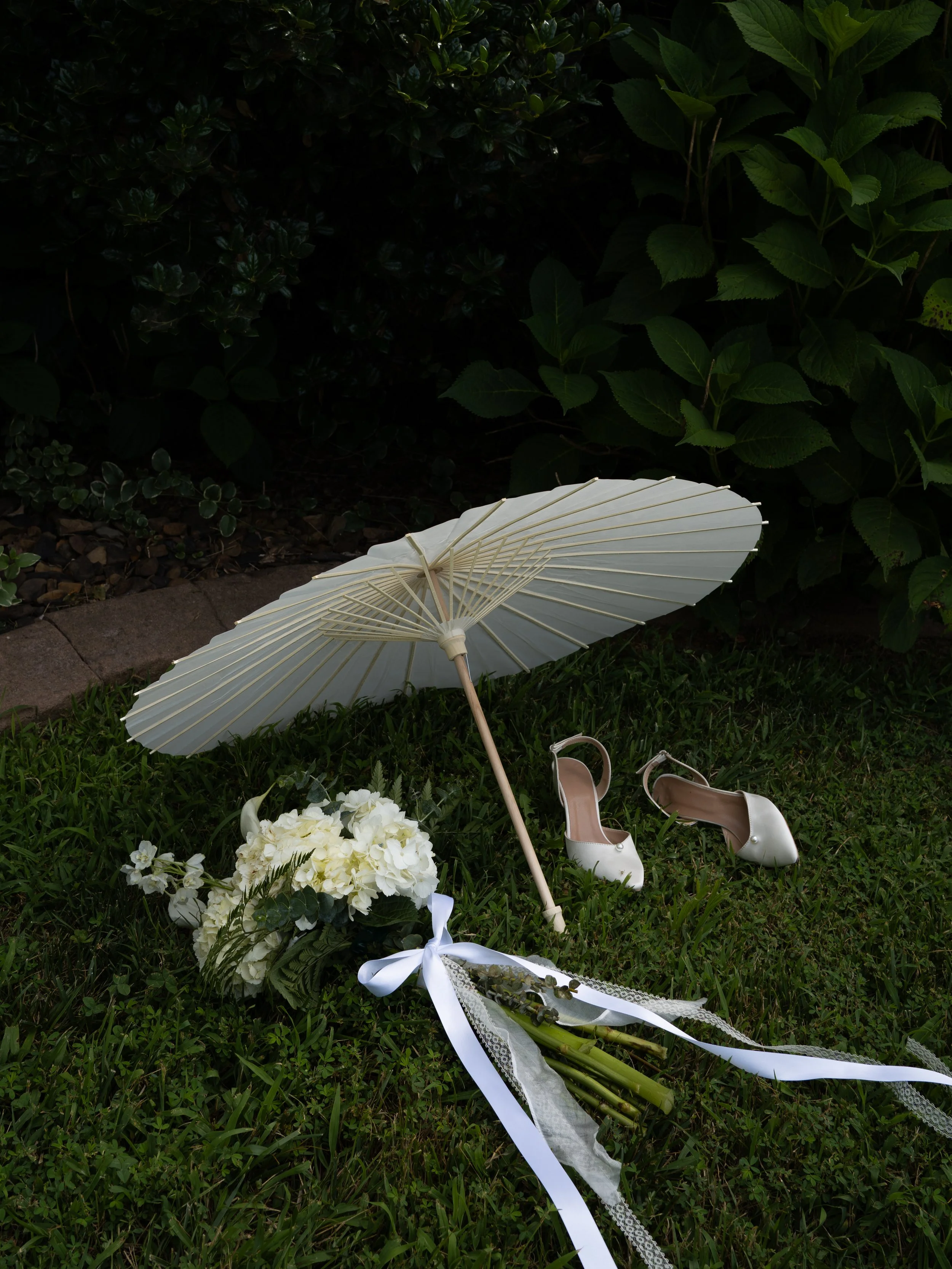 Bride wedding detail lay with shoes, bouquet, and parasol.