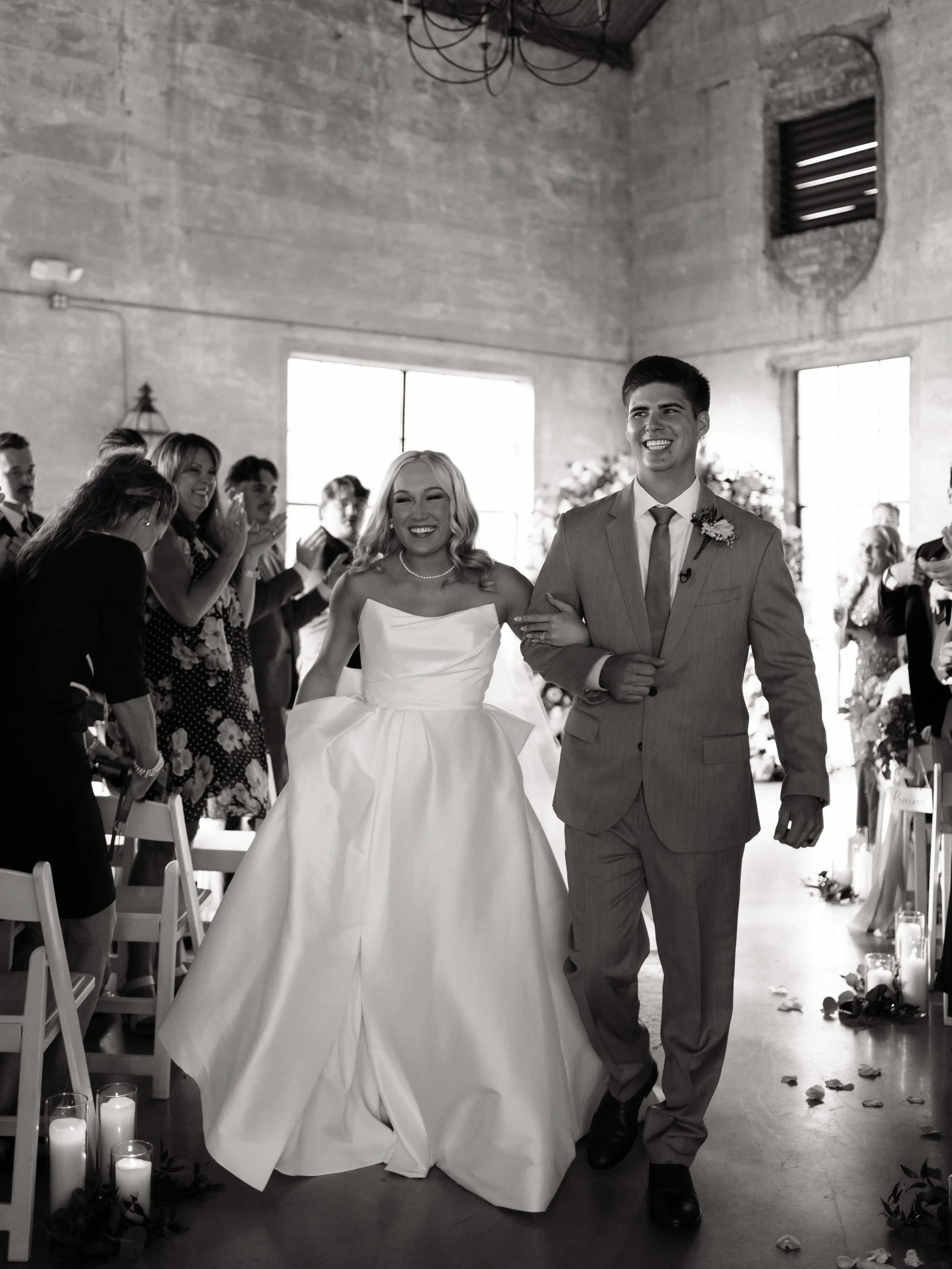 The newly married couple walks down the aisle in Montgomery, TX, surrounded by loved ones in a timeless black-and-white frame.