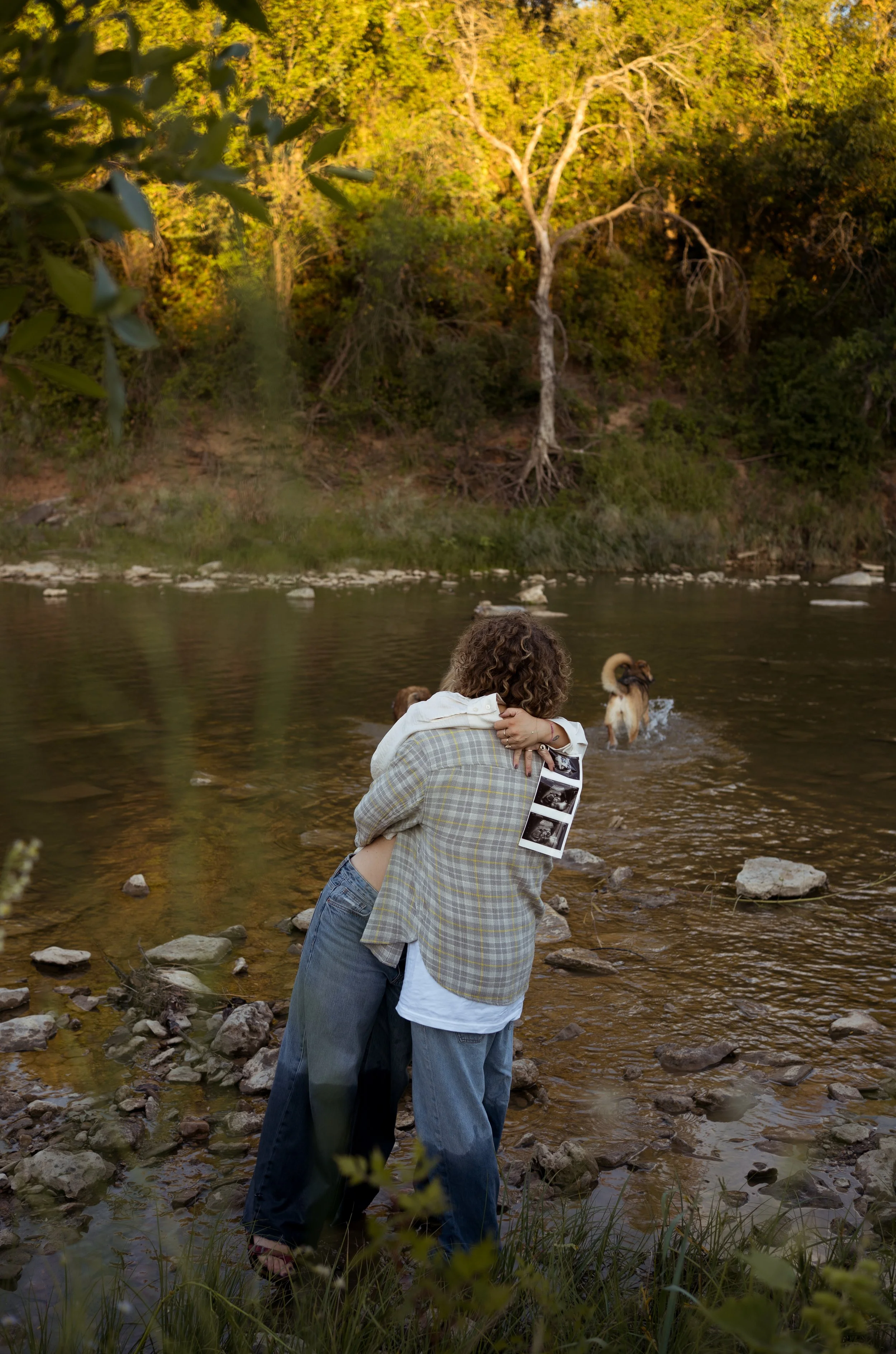 A heartfelt moment in Rainbow, Texas, as the couple embraces by the water, holding ultrasound images.