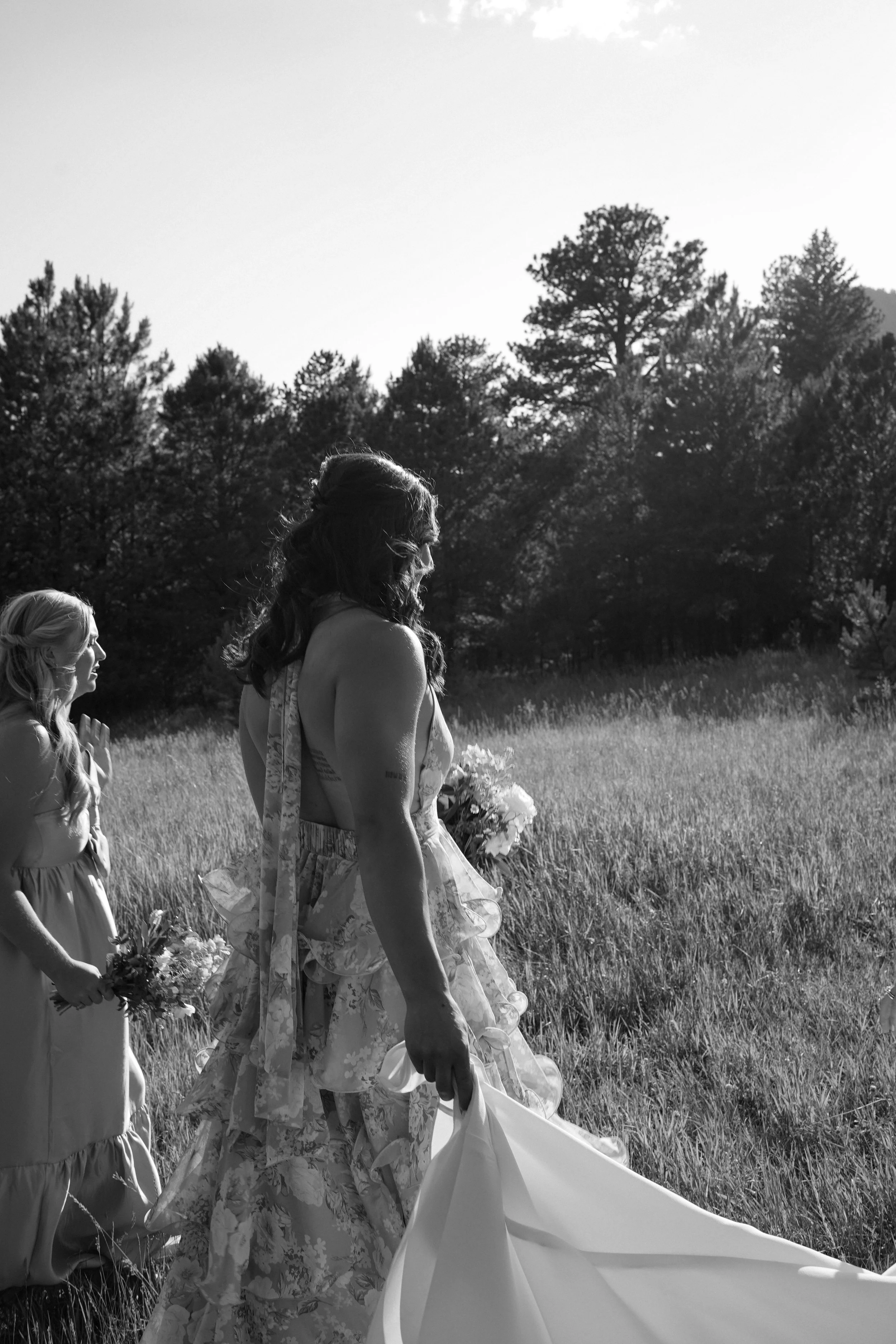 Black and white candid of bridesmaids walking together through a field during a Pine, Colorado wedding.