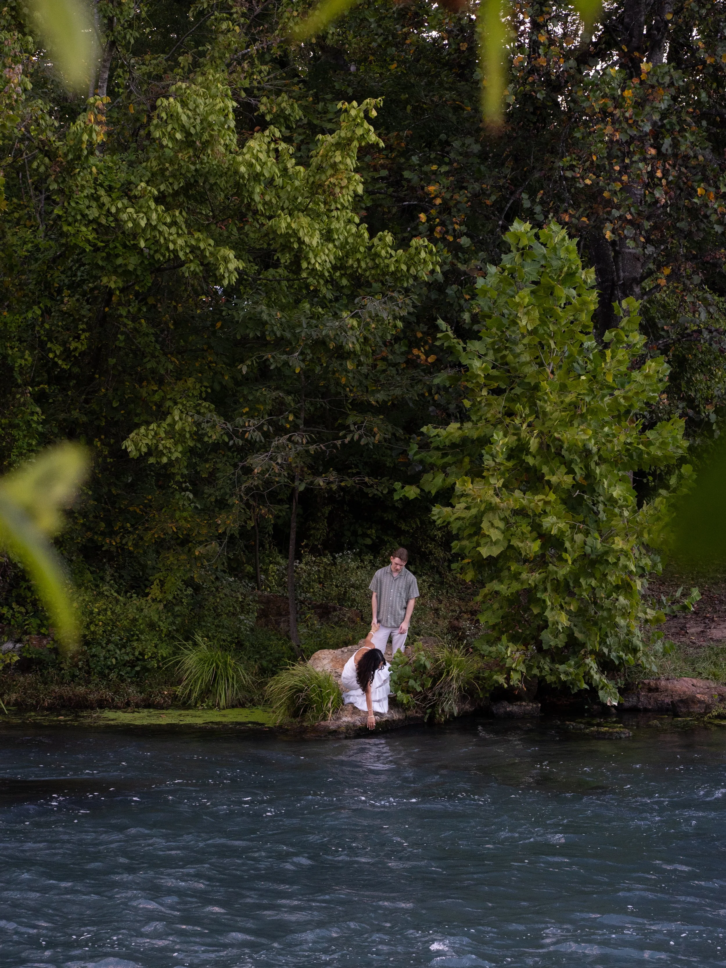 Couple standing near a flowing spring river surrounded by lush greenery during an engagement session in Mammoth Spring Arkansas